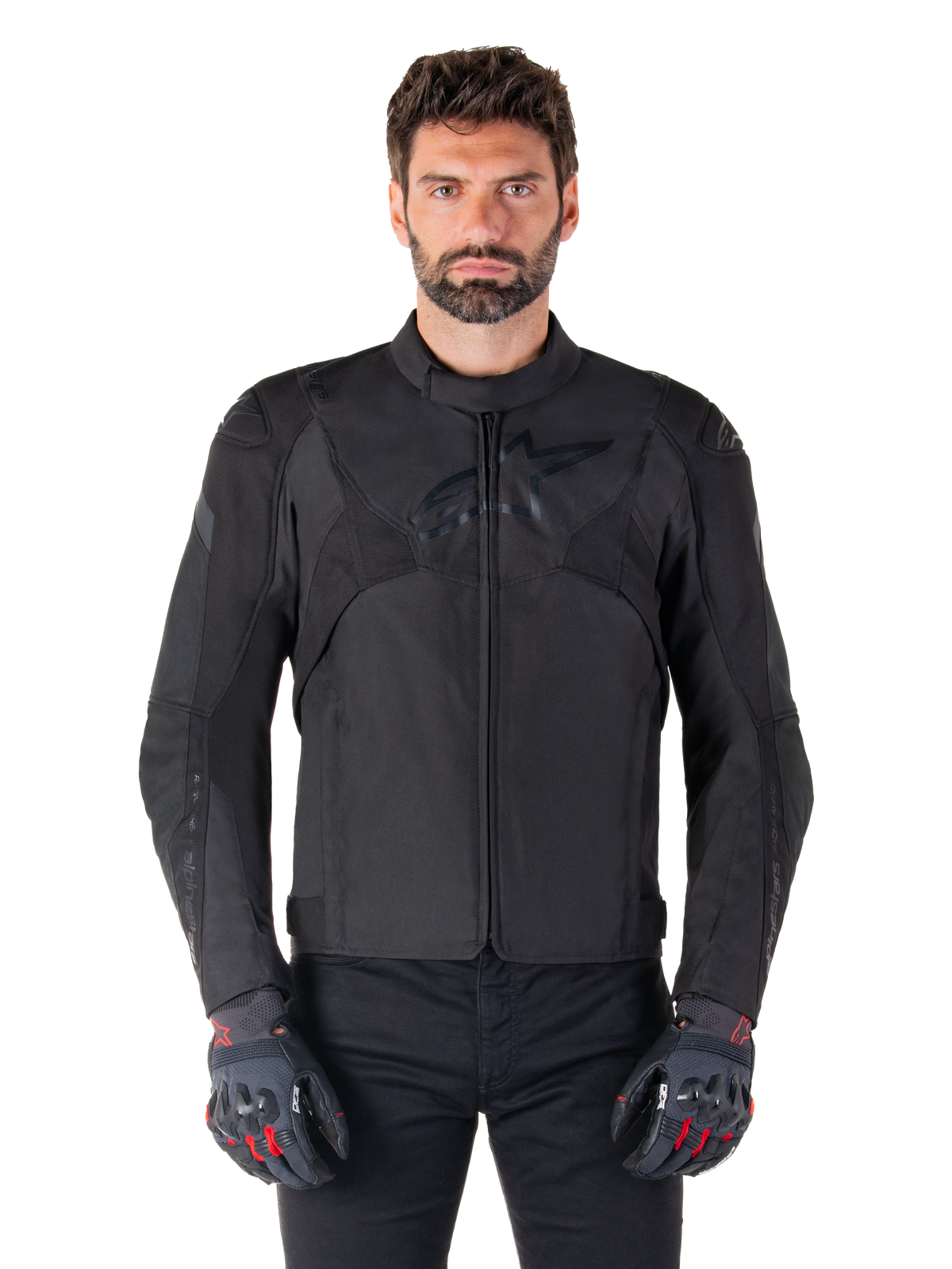 Alpinestars T-Jaws V4 vandtæt jakke, sort motorcykel sportsjakke, bæres af en mand med sorte handsker med røde detaljer, forstærkede skuldre og arme, strømlinet design med diskret logo på brystet, tekstilkøreudstyr til al slags vejr