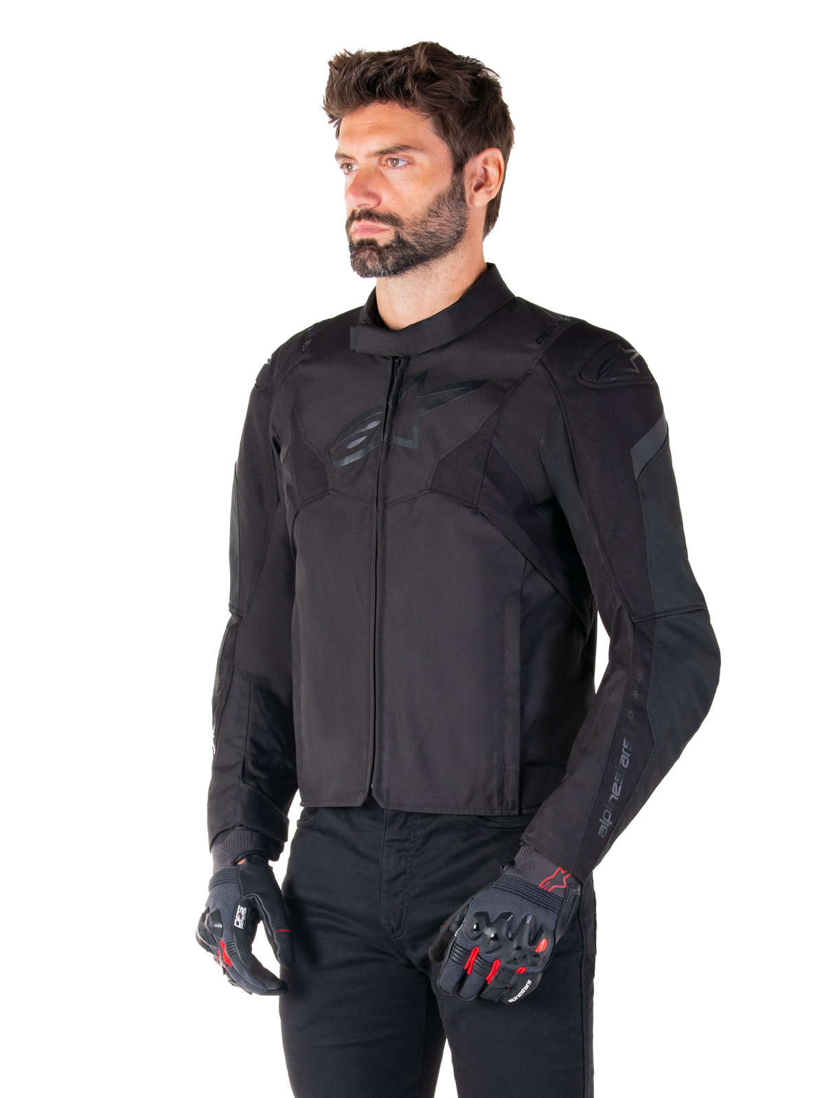 Mandlig motorcyklist iført Alpinestars T-Jaws V4 Waterproof Jacket i Black Black, kombineret med sorte bukser og beskyttelseshandsker, med en slank sportspasform, tonale Alpinestars-logoer på brystet og skuldrene og en højtydende tekstilkonstruktion.