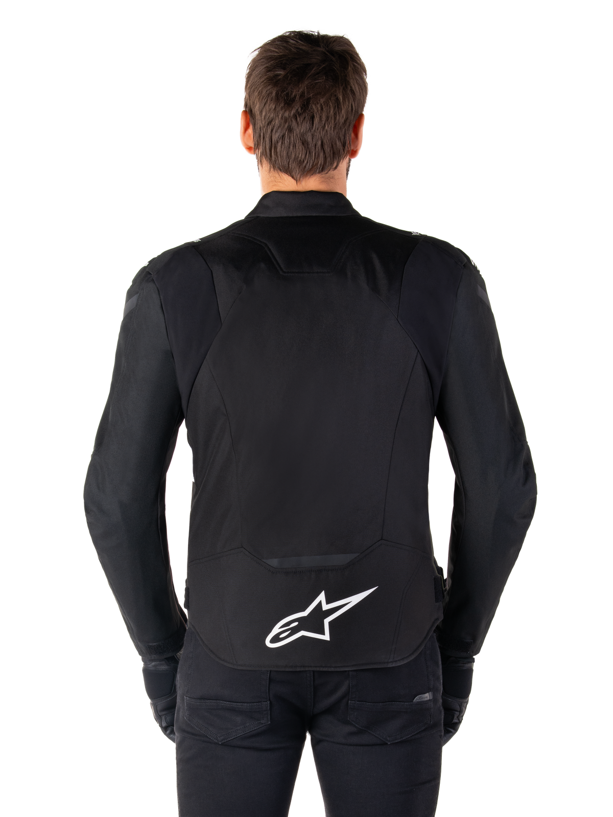 Alpinestars T-Jaws V4 Waterproof-jakke, sort motorcykeljakke set bagfra, med hvidt Alpinestars-logo på lænden, forlænget ryg for dækning, båret af model med sorte bukser og handsker, strømlinet sportstekstildesign