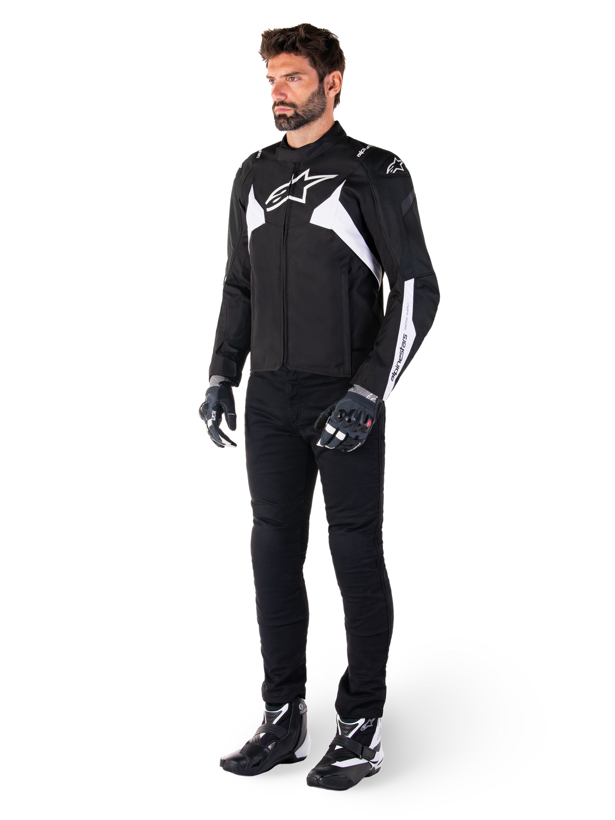 Mandlig model iført Alpinestars T-Jaws V4 vandtæt jakke i sort og hvid, sports-tekstiljakke med hvidt stjernelogo og detaljer på ærmerne, stylet med sorte motorcykelbukser, handsker og støvler for et komplet look til landevejskørsel.