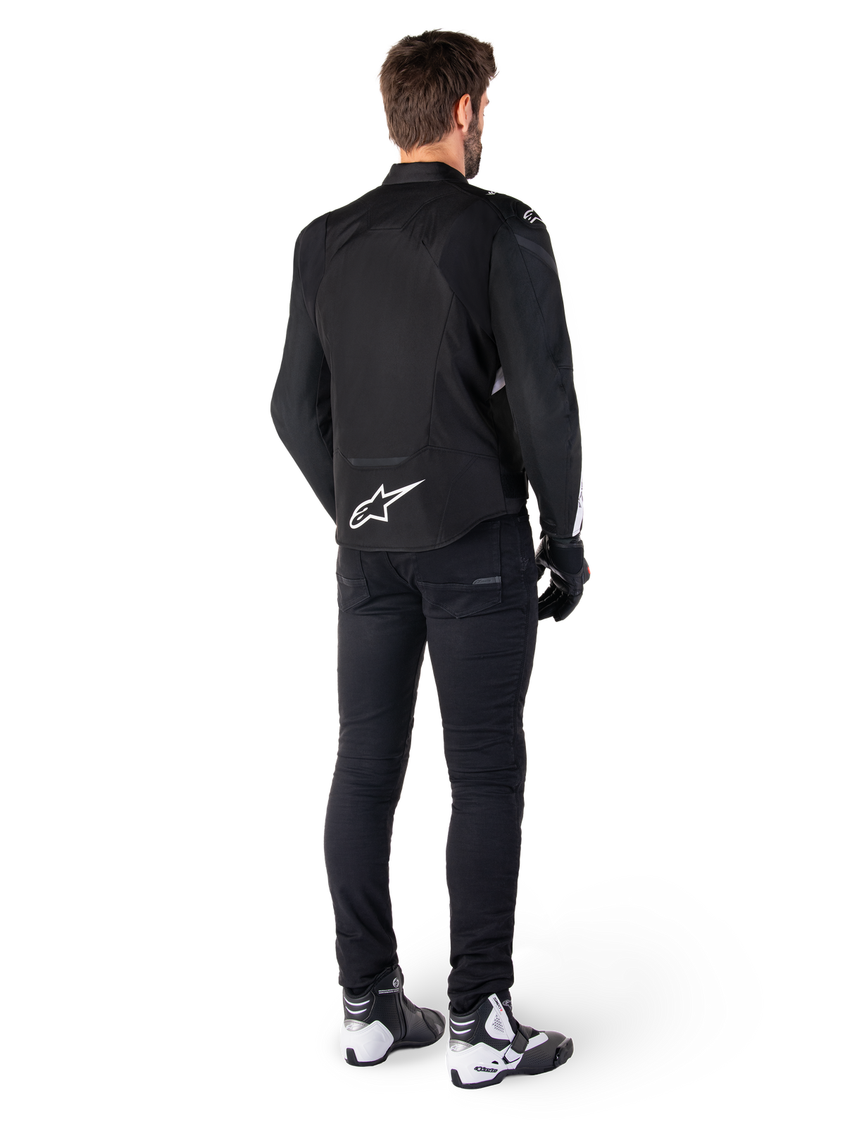 Alpinestars T-Jaws V4 vandtæt jakke, sort og hvid, set bagfra med hvidt stjernelogo nederst på ryggen, båret af model med sorte motorcykelbukser, sorte handsker og hvid-sorte motorcykelstøvler.