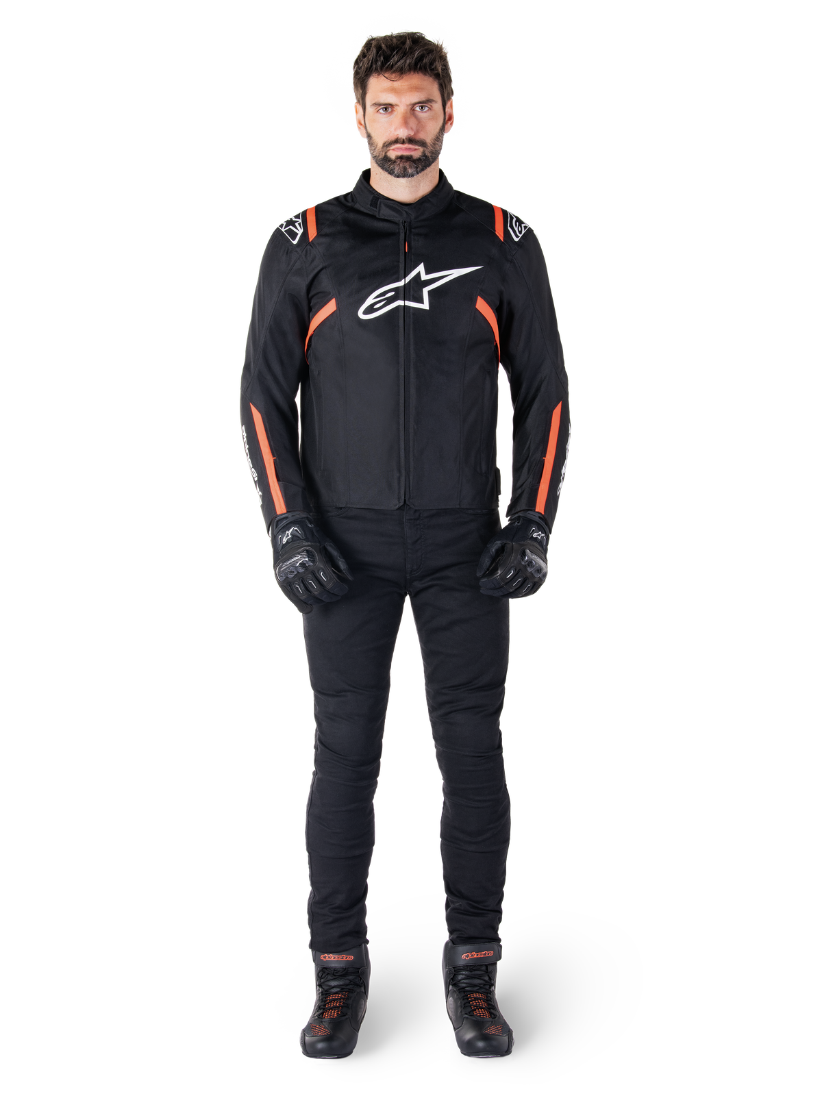 Male model wearing the Alpinestars T-SPS V2 Waterproof Jacket in Black White Red Fluo, paired with black motorcycle pants and gloves, featuring a white Alpinestars logo on the chest and red accents on the sleeves.
