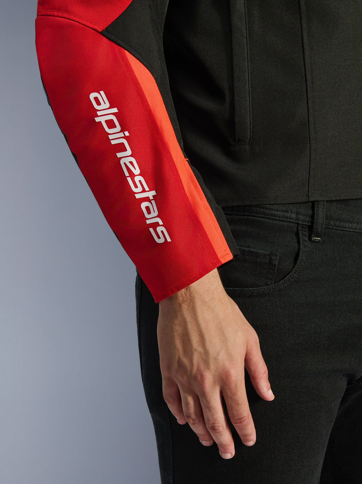 Alpinestars T-SPS V2 vandtæt jakke, motorcykeljakke, sort og rød, nærbillede af ærmet med et hvidt lodret brandlogo på et rødt panel, holdbar tekstilkonstruktion med et sportsinspireret design