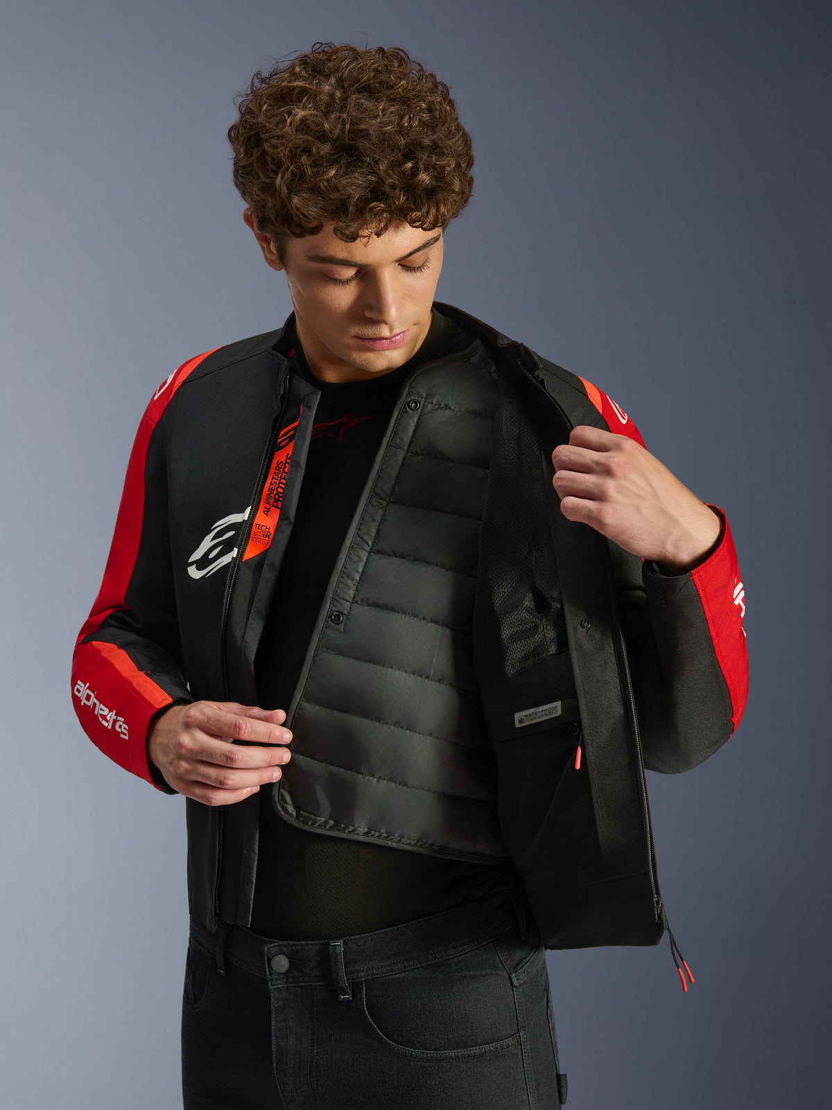 Alpinestars T-SPS V2 vandtæt jakke, sort og rød, med en model, der viser det indvendige quiltede termiske for og det vandtætte rum, Tech-Air Ready-branding på indersiden, motorcykeljakke i sportssnit.