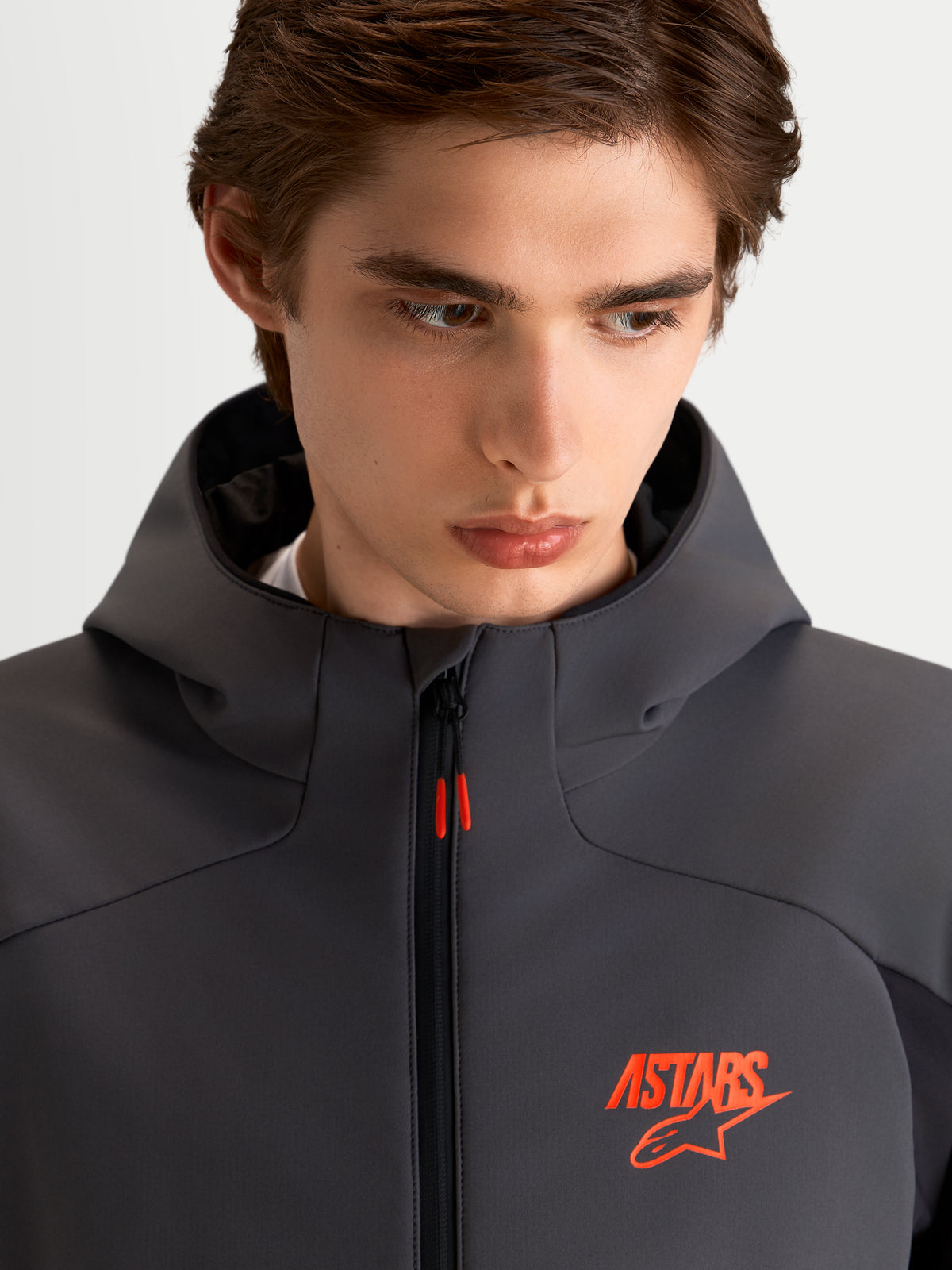 Alpinestars Aeroshell Waterproof Jacket, herre-motorcykeljakke i sort og mørk grå softshell, med hætte og orange ASTARS-logo, nærbillede af model