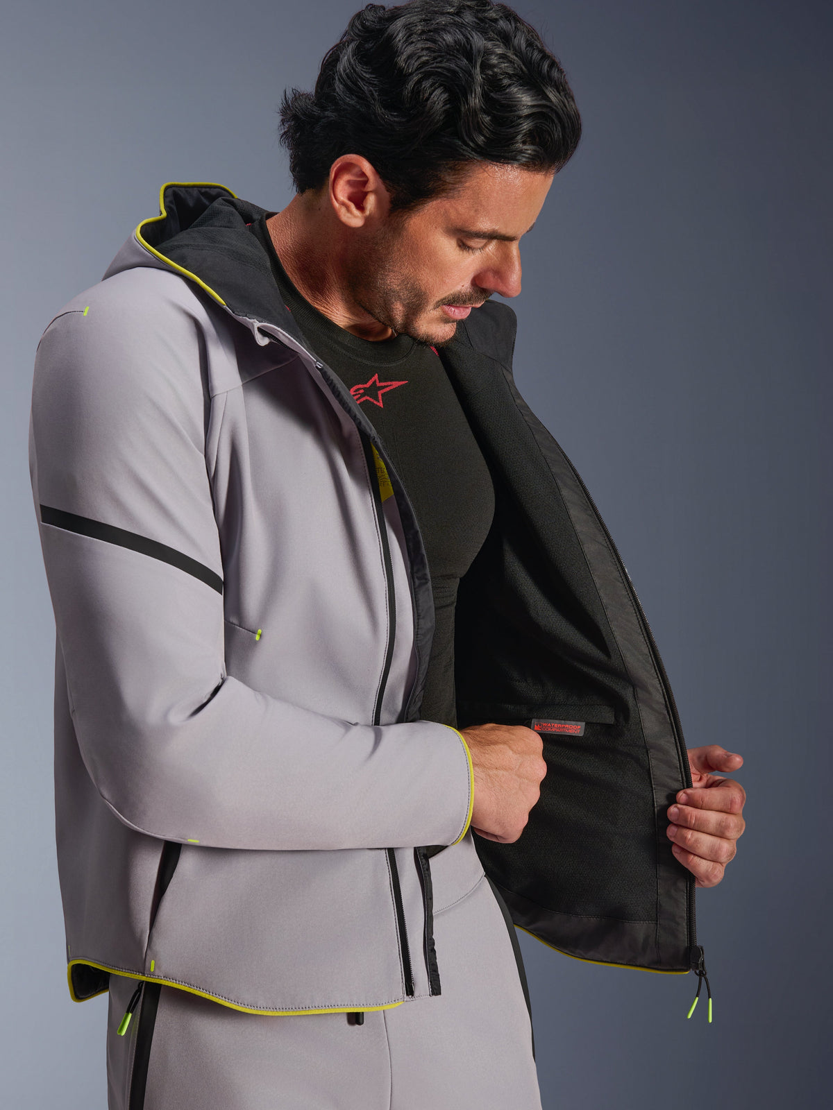 Alpinestars Aeroshell Waterproof Jacket in Mid Gray and Yellow Fluo, worn by a male model showing the internal waterproof compartment and black lining, sports softshell motorcycle hoodie with fluorescent yellow trim and modern athletic fit.