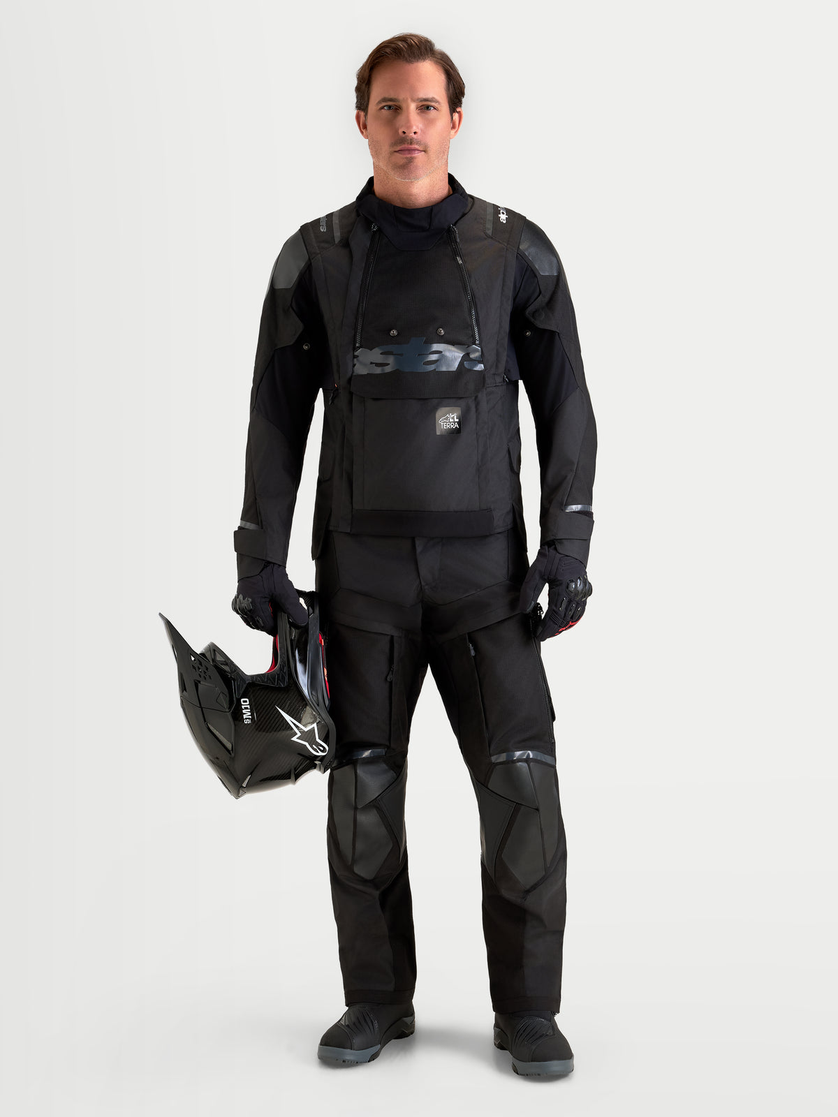 Alpinestars Harok V2 Drystar herre-motorcykeljakke i sort, båret med matchende kørebukser og med en hjelm i hånden, vandtæt tekstilkonstruktion og modulær ventilation