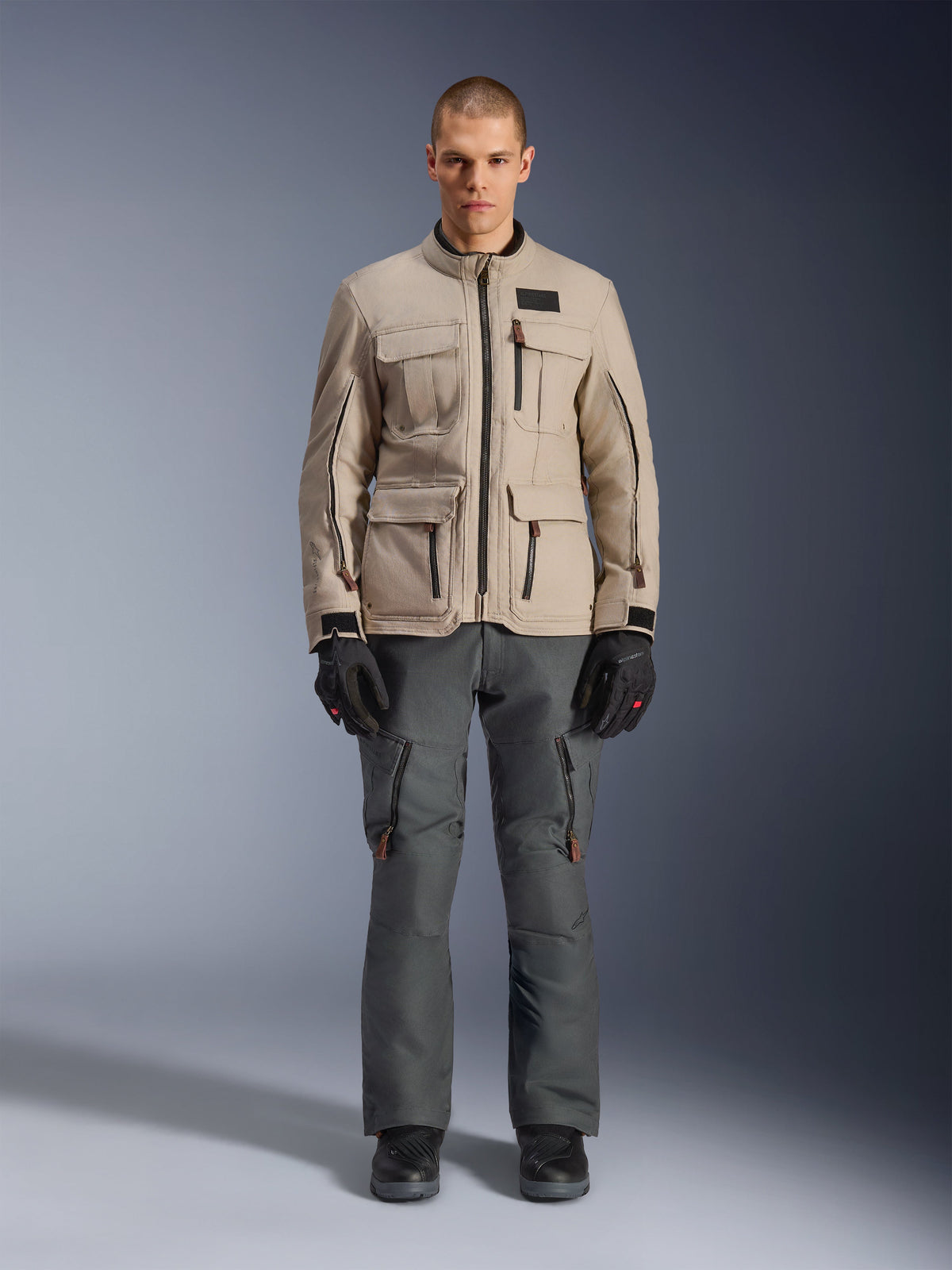 Alpinestars Borrego Drystar® Jacket, Adventure Motorcycle Jacket, Warm Gray, worn by a model with dark gray riding pants and black gloves, featuring multiple cargo pockets and a durable textile construction with a classic waxed-canvas look.
