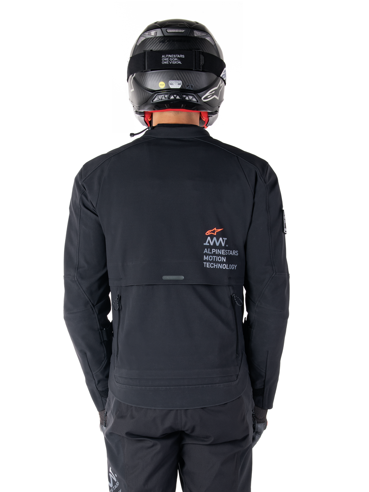 Alpinestars AMT-8 Stretch Drystar® XF jakke, set bagfra, sort, båret med sort hjelm og bukser, med Alpinestars Motion Technology-branding på ryggen, adventure touring-design med ergonomisk strækmateriale.