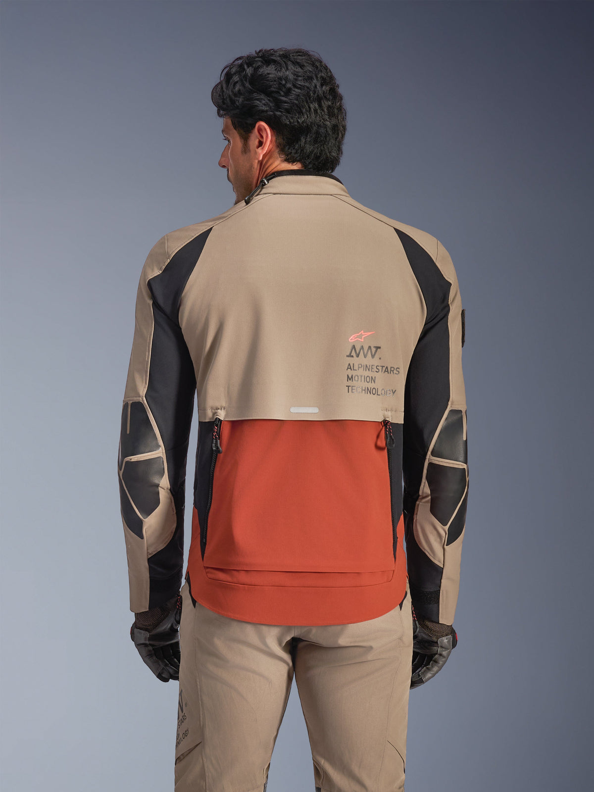 Alpinestars AMT-8 Stretch Drystar® XF Jakke, Walnut Rust Black, set bagfra på model, fremhæver bagudstødningen med skifertag-design i rust, valnøddebrune øverste sektioner, sorte detaljer på ærmerne og Alpinestars Motion Technology-branding