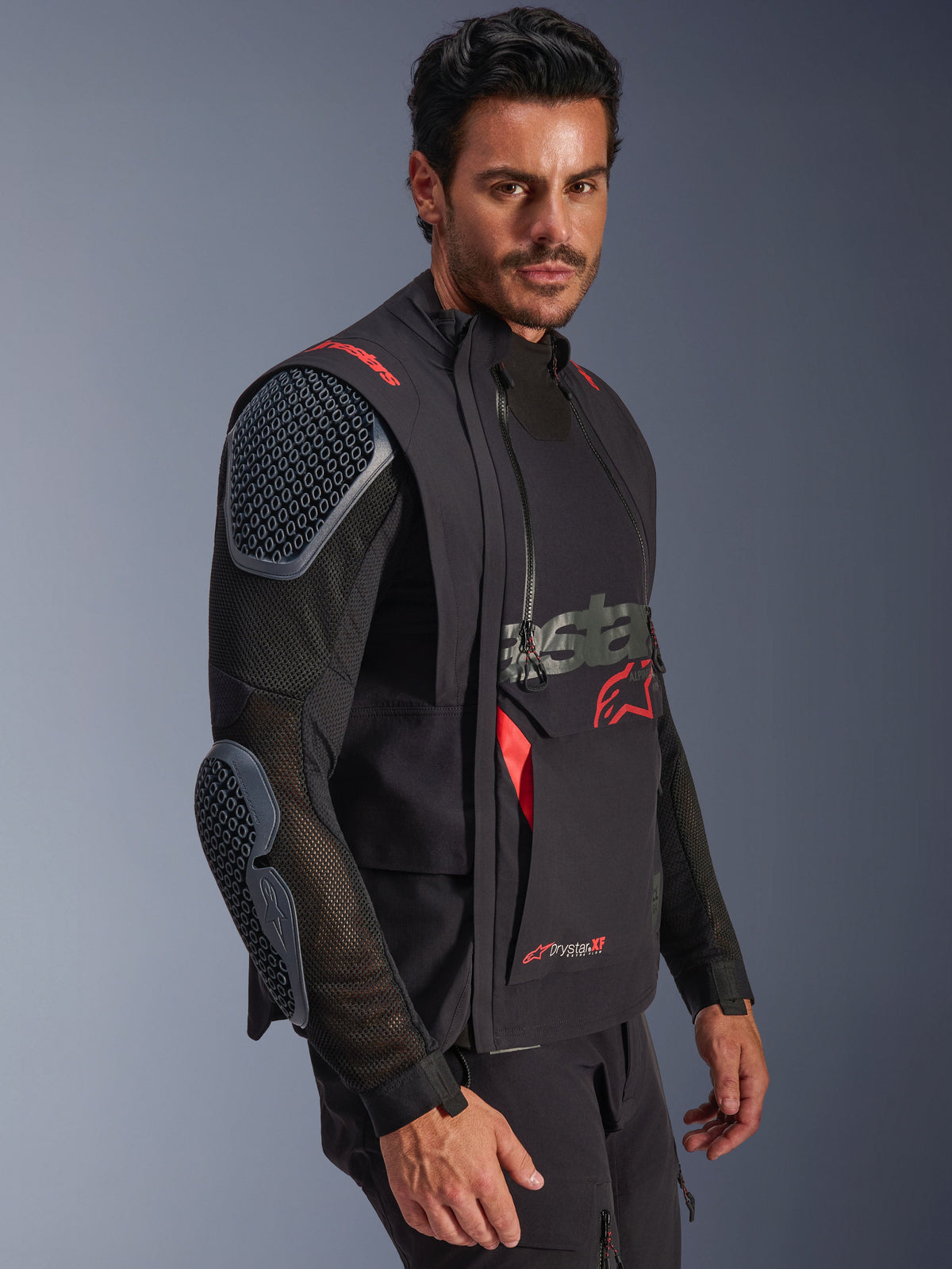 Alpinestars Halo Pro Drystar® XF lamineret jakke, Black og Dark Shadow, adventure-motorcykeljakke båret af model, modulær konfiguration med mesh-ærmer og integreret skulder- og albuebeskyttelse, røde logodetaljer og tekniske vandtætte lynlåse.