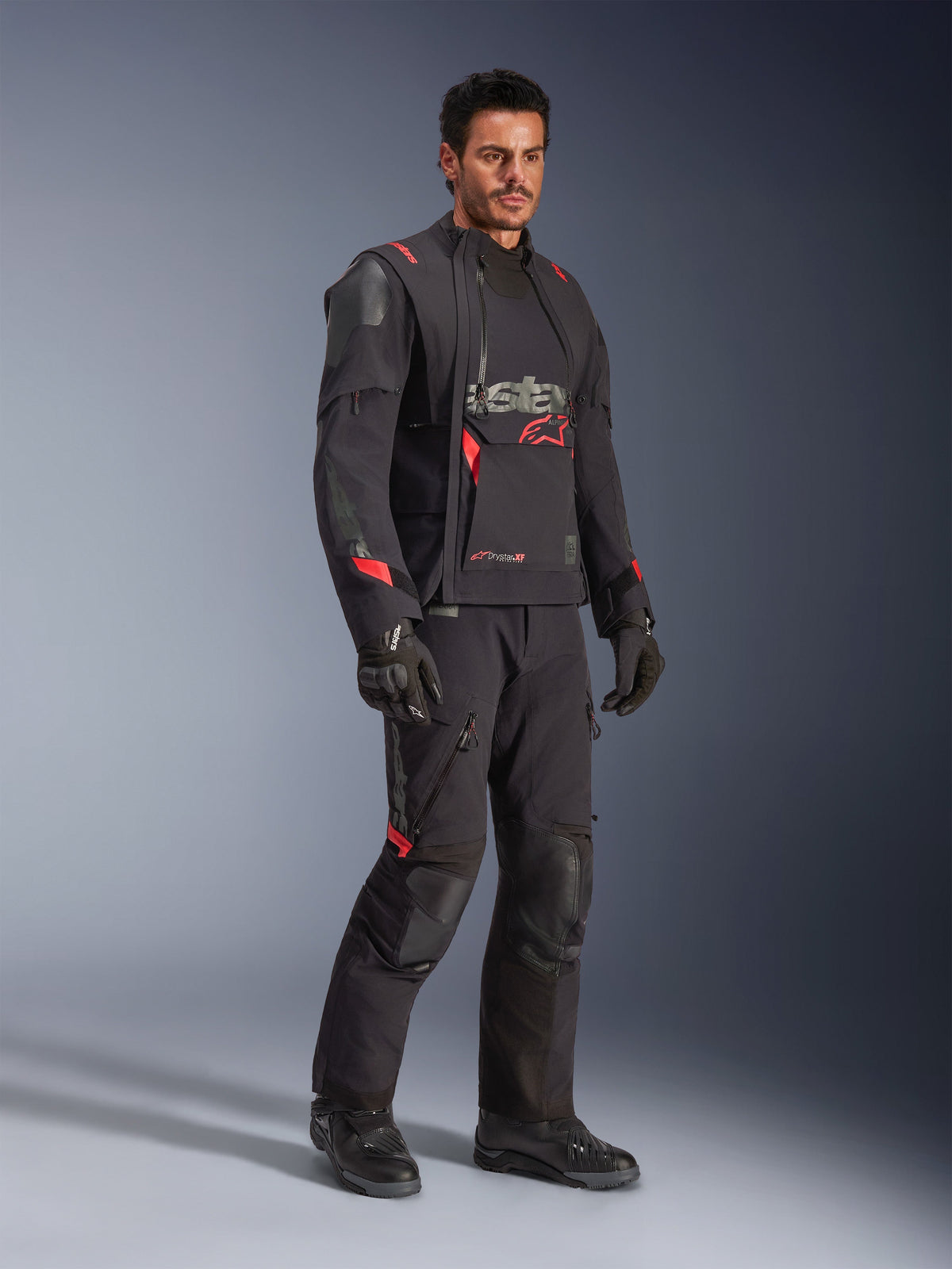 Mandlig kører iført Alpinestars Halo Pro Drystar® XF lamineret jakke i Black Dark Shadow, komplet adventure-køreudstyr med matchende bukser, handsker og støvler, med modulære asymmetriske frontpaneler og røde branding-detaljer.
