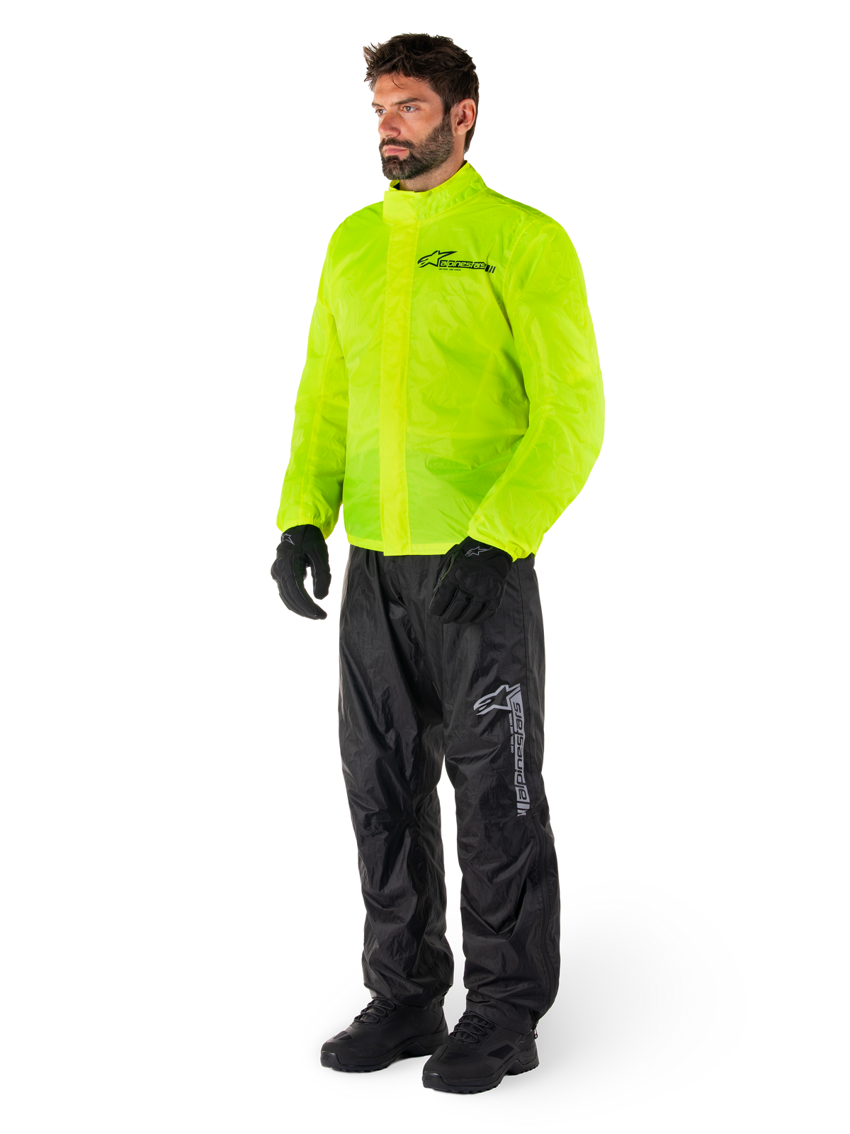 Mand iført Alpinestars Hurricane Rain V2-jakke i Yellow Fluo og Hurricane Rain V2-bukser i sort, vandtæt motorcykelregntøj med høj synlighed, reflekterende logoer på bryst og lår, komplet outfit med sorte handsker og støvler