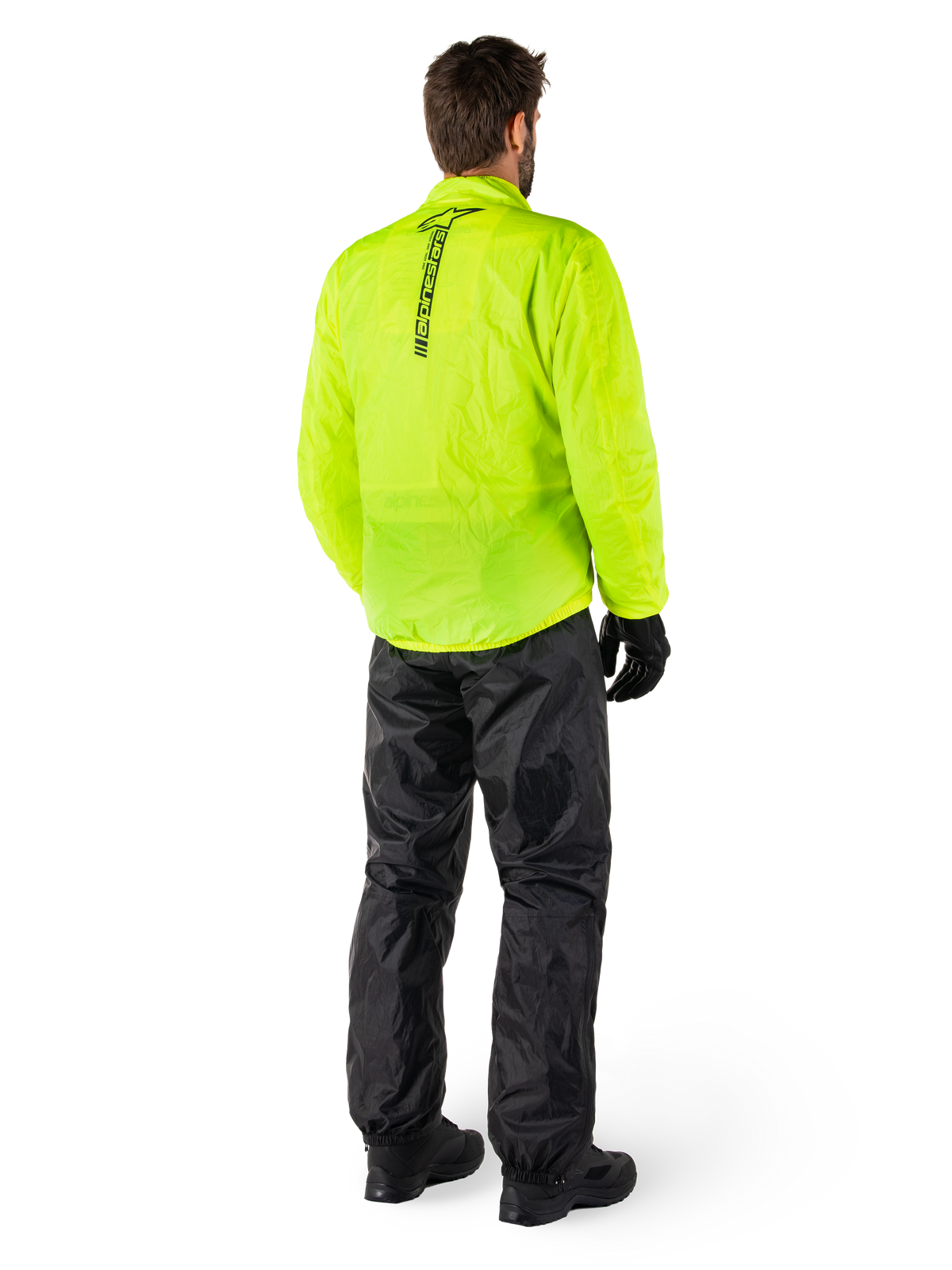 Person set bagfra iført Alpinestars Hurricane Rain V2-jakke i Yellow Fluo og Hurricane Rain V2-bukser i sort, lodret logo på ryggen, vandtæt motorcykelregntøj med sorte handsker og støvler