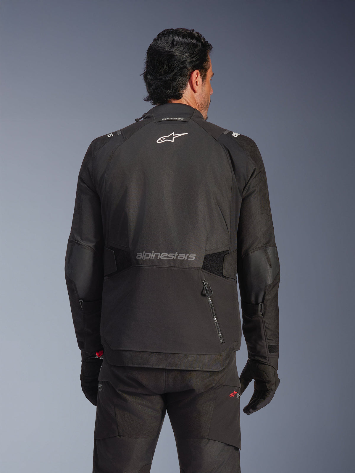 Alpinestars Andes V4 Drystar®-jakke, sort, bagsidevisning på en model, tekstil adventure-jakke med reflekterende logoer og en baglomme med lynlås, stylet med matchende sorte bukser og handsker