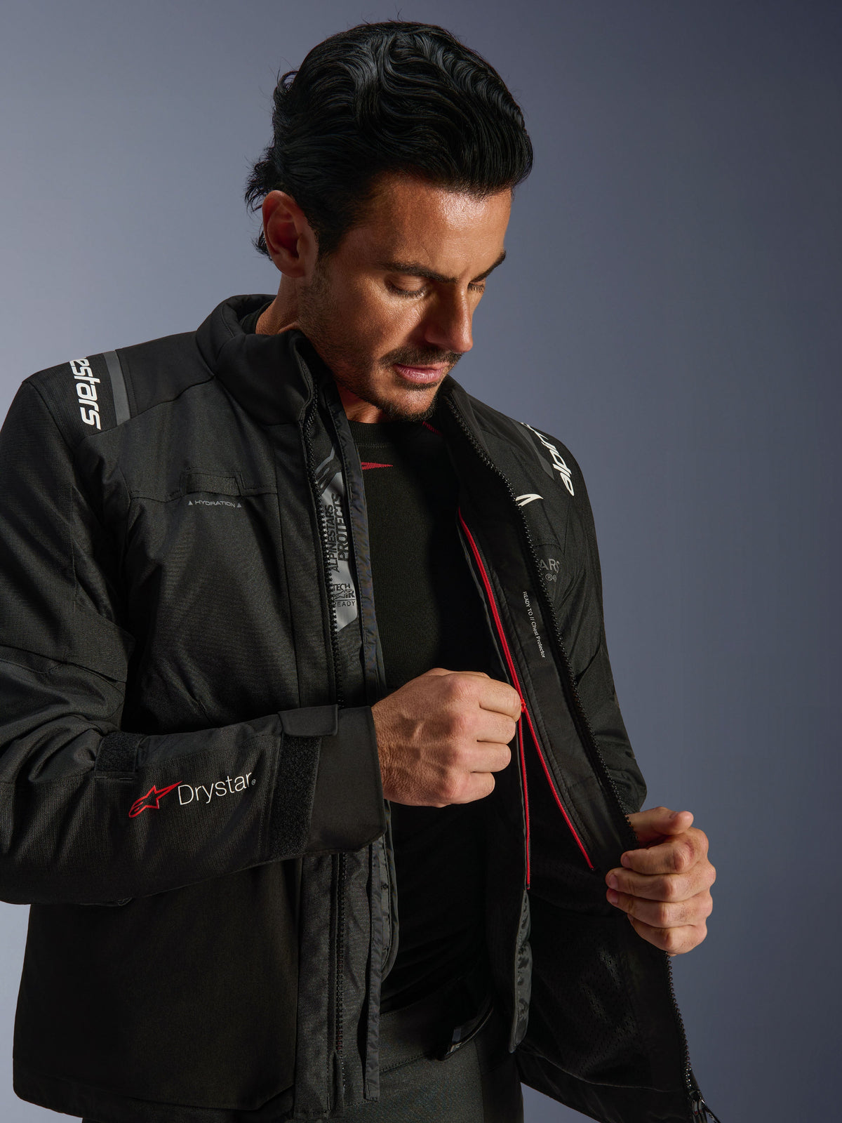 Alpinestars Andes V4 Drystar® jakke, sort adventure-motorcykeljakke, mand der demonstrerer den indvendige termoforing og den røde lynlås, med Drystar®-branding på ærmet, slidstærkt tekstilmateriale til kørsel i al slags vejr