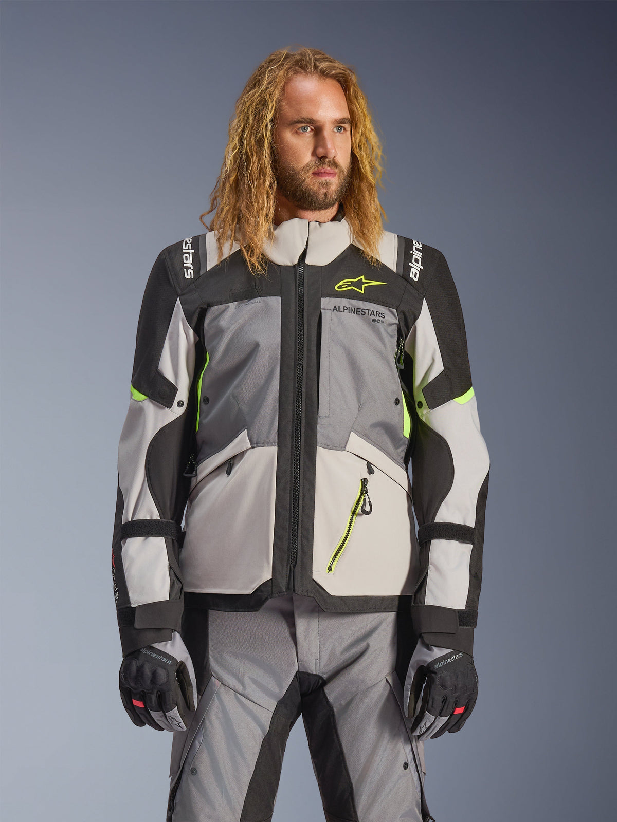 Alpinestars Andes V4 Drystar Jacket, Adventure Touring Motorcycle Jacket, Dark Gray and Ice Gray with Neon Yellow accents, worn by a model with matching pants and gloves, multi-pocket textile design for all-weather riding