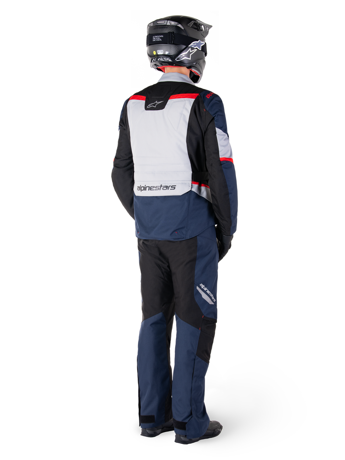 Rear view of a rider wearing the Alpinestars ST-1 Waterproof Jacket in Dark Blue Black Bright Red, paired with matching waterproof pants and a black helmet, featuring a prominent grey back panel with Alpinestars branding and an adventure touring design.