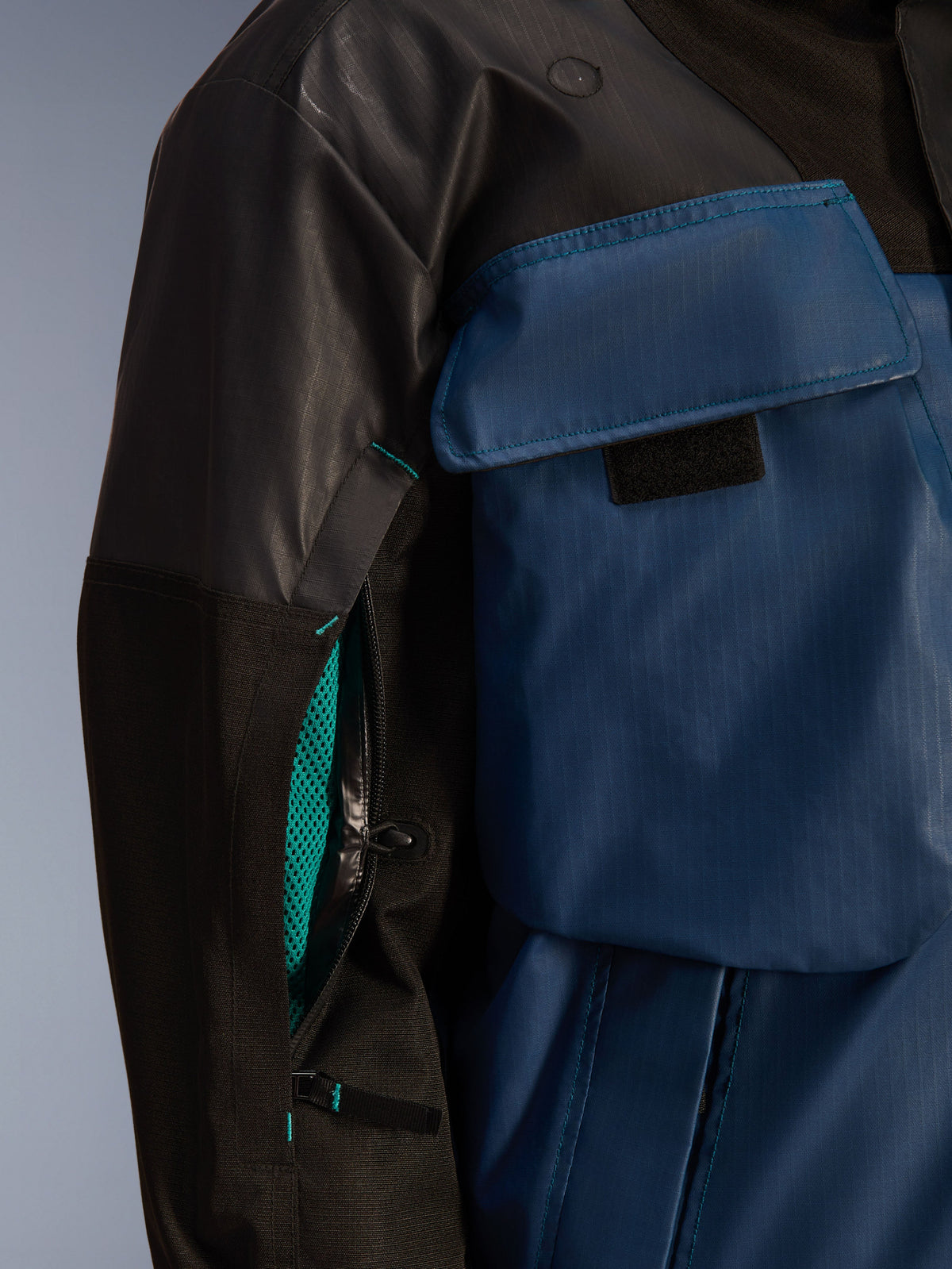 Close-up of Alpinestars Mospher WP Jacket in Black and Dark Petrol, featuring an open sleeve ventilation zipper with bright teal mesh lining, large chest pocket, and durable ripstop textile material.