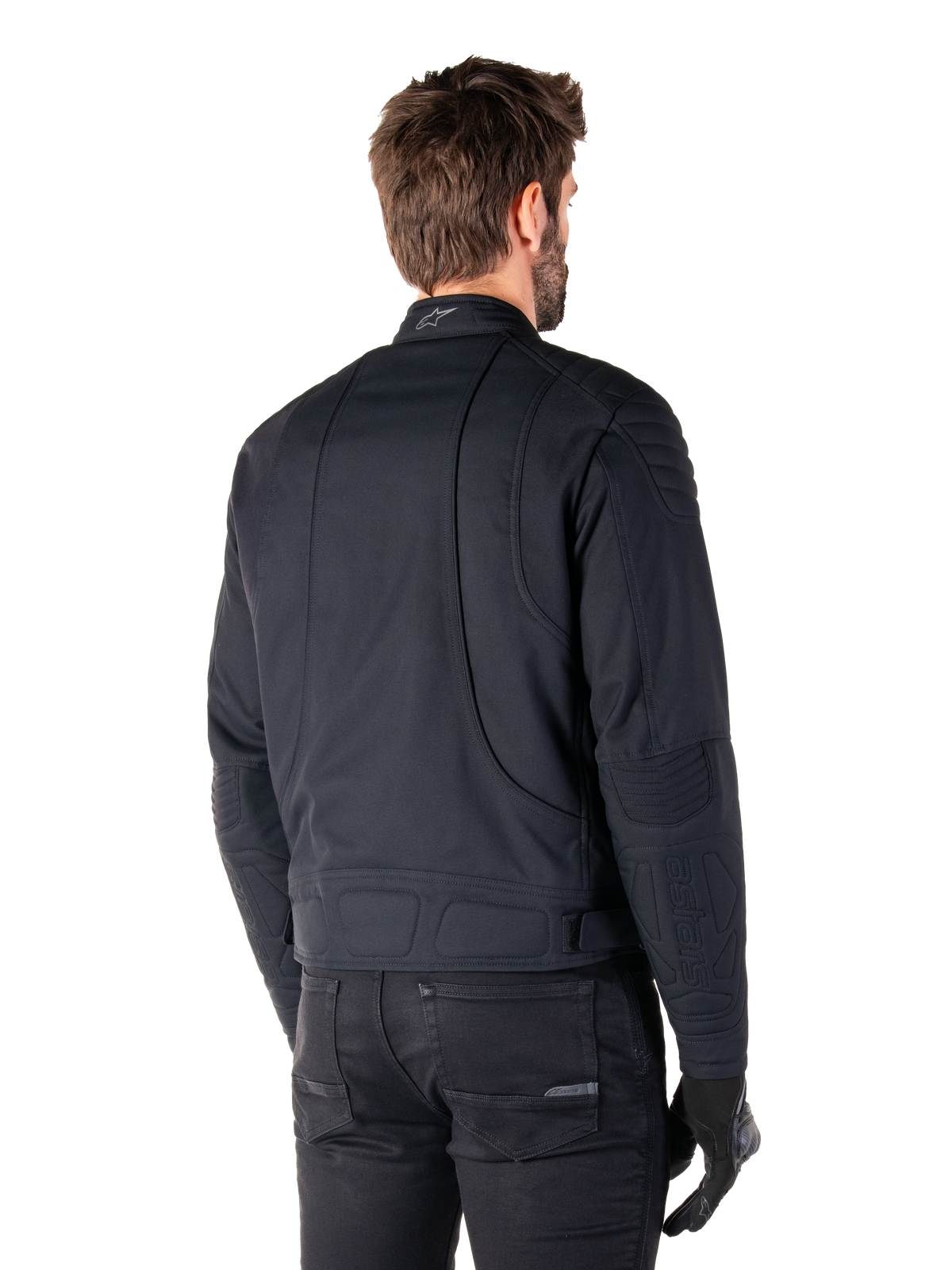 Alpinestars Clayton WR Jakke i sort, trekvart visning bagfra på en mandlig model, urban motorcykeljakke med quiltet polstring på skuldre og albuer, tekniske syninger og reflekterende logo på kraven, stylet med sorte bukser og handsker.