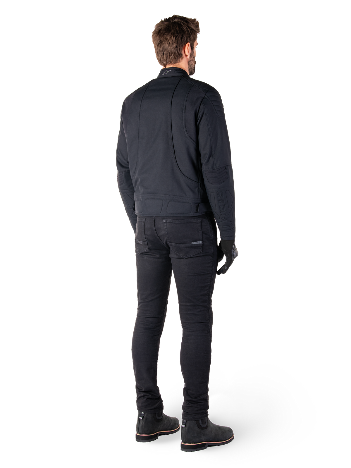 Alpinestars Clayton WR-jakke i sort, set bagfra af en kører, med quiltede albue- og skulderpaneler, ergonomiske buede syninger, reflekterende detaljer på kraven, sorte kørebukser og støvler, urbant motorcykel-look.