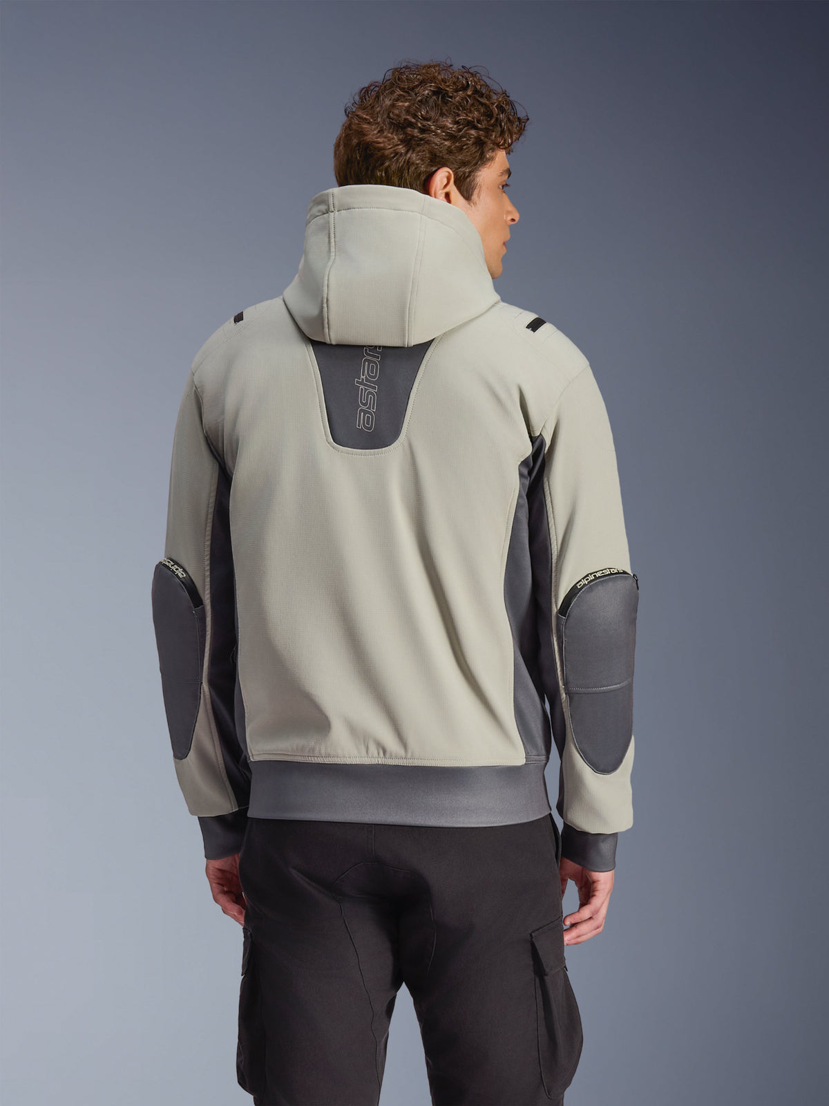 Alpinestars Moblast vandtæt jakke i Iron Gray og Dark Sage, set bagfra på model, urban motorcykeljakke med hætte, mørkegrå stretchpaneler og forstærkede albuer, kombineret med sorte cargobukser