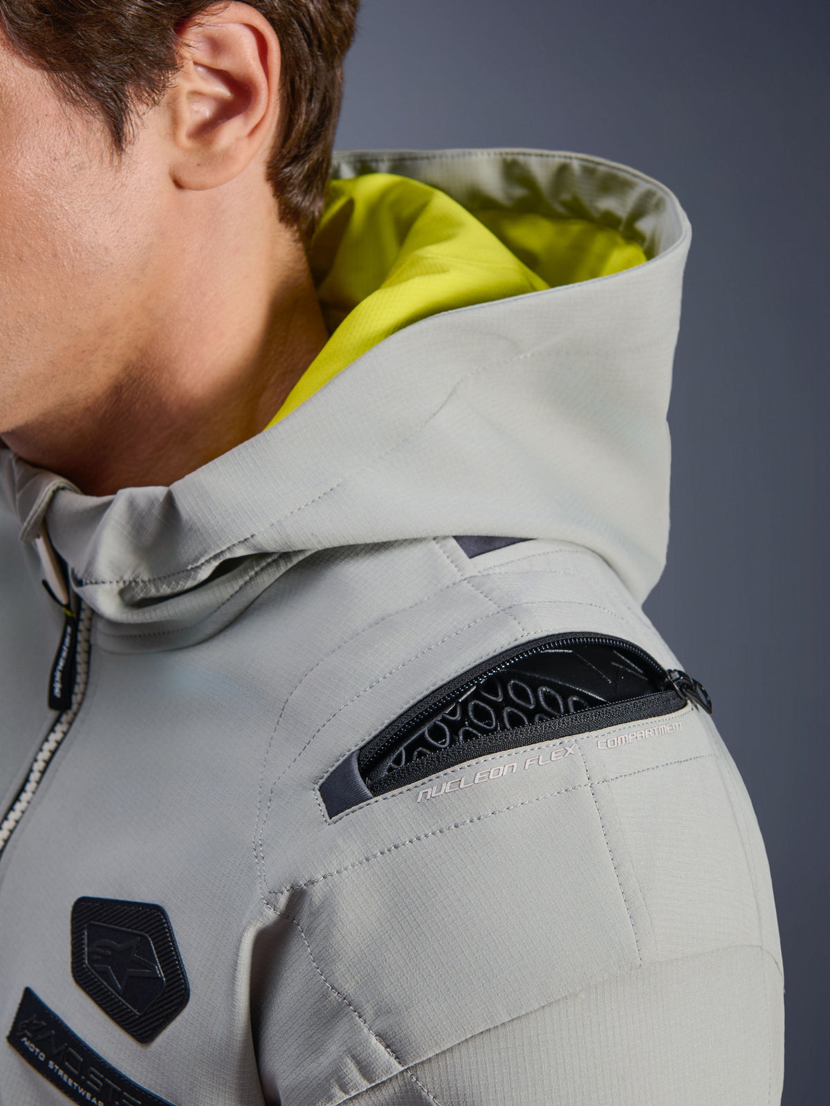 Alpinestars Moblast WP Jacket, Iron Gray, nærbillede af skulder der viser åbent Nucleon Flex-beskytterrum, neongul indvendig hætte, teknisk urbant motorcykeludstyr med funktionelle lynlåse