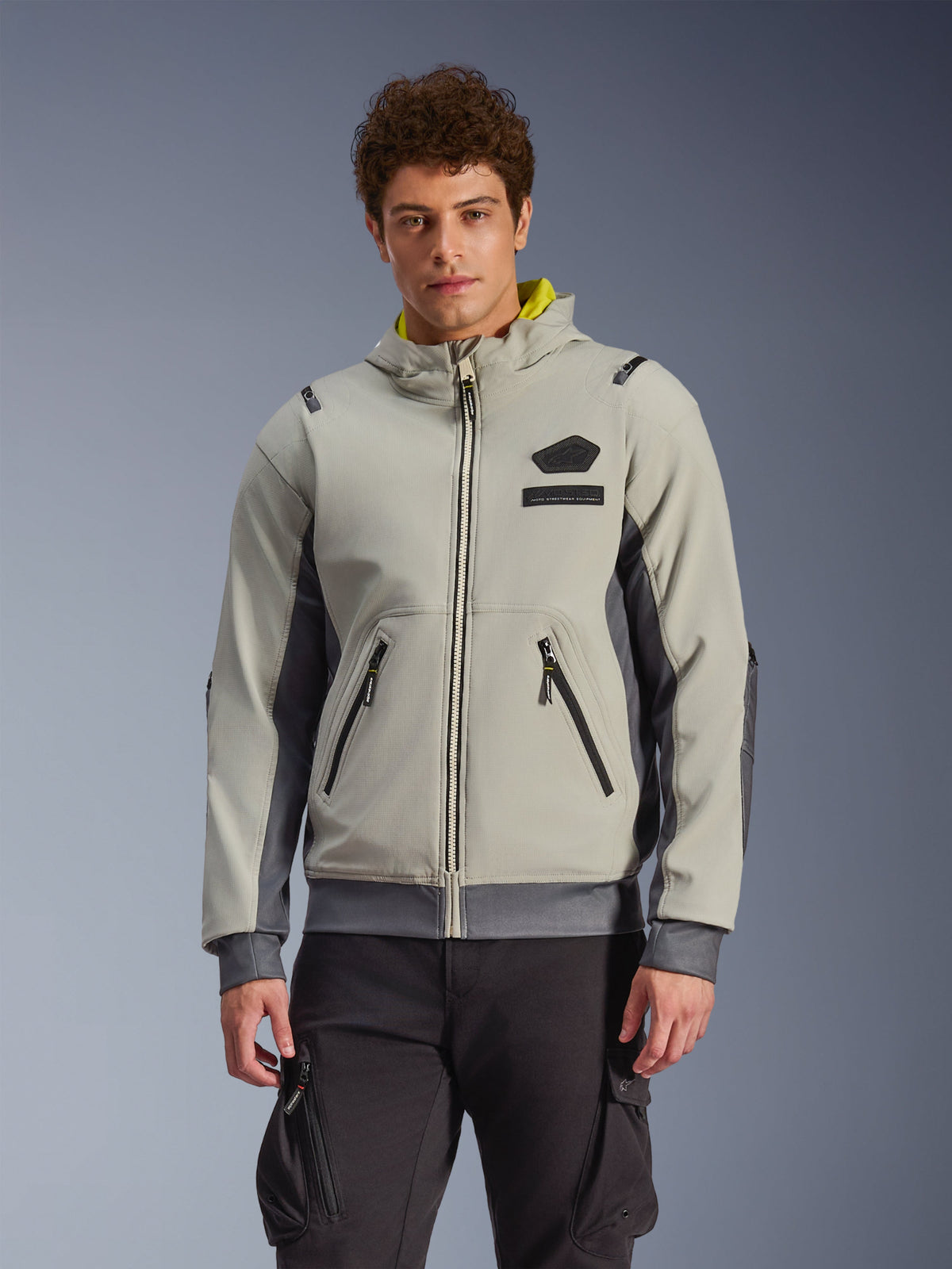 Alpinestars Moblast vandtæt jakke, lysegrå og mørkegrå urban motorcykel-hættetrøje med gult hættefoer, forlommer og sorte lynlåse, båret med sorte cargobukser, moderne sporty design