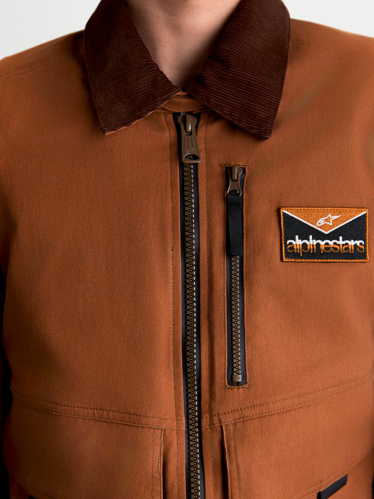 Alpinestars Mustang WP jakke, herre urban motorcykeltekstiljakke i mørk rust og mørkebrun, nærbillede af stretch twill-konstruktion i workwear-stil, fløjlskrave, lynlås foran og logomærke på brystet
