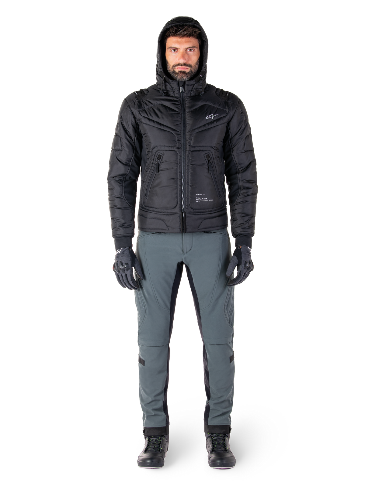 Alpinestars Mohobbs Waterproof-jakke i sort, mandlig model iført quiltet, polstret bomberjakke med hætte, kombineret med grå kørebukser, sorte handsker og sorte støvler, moderne urbant motorcykeludstyr