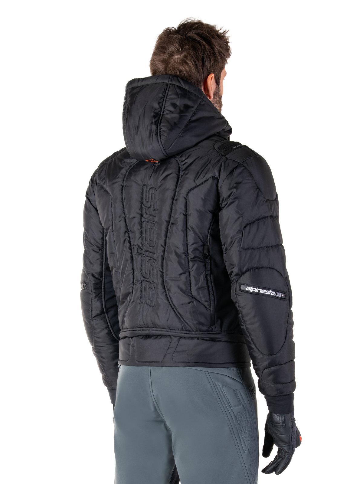 Alpinestars Mohobbs vandtæt jakke, sort, set bagfra med quiltet polstret konstruktion, hætte, lodret astars-ordmærke på ryggen, Alpinestars-branding på ærmerne, båret med grå bukser og sorte handsker