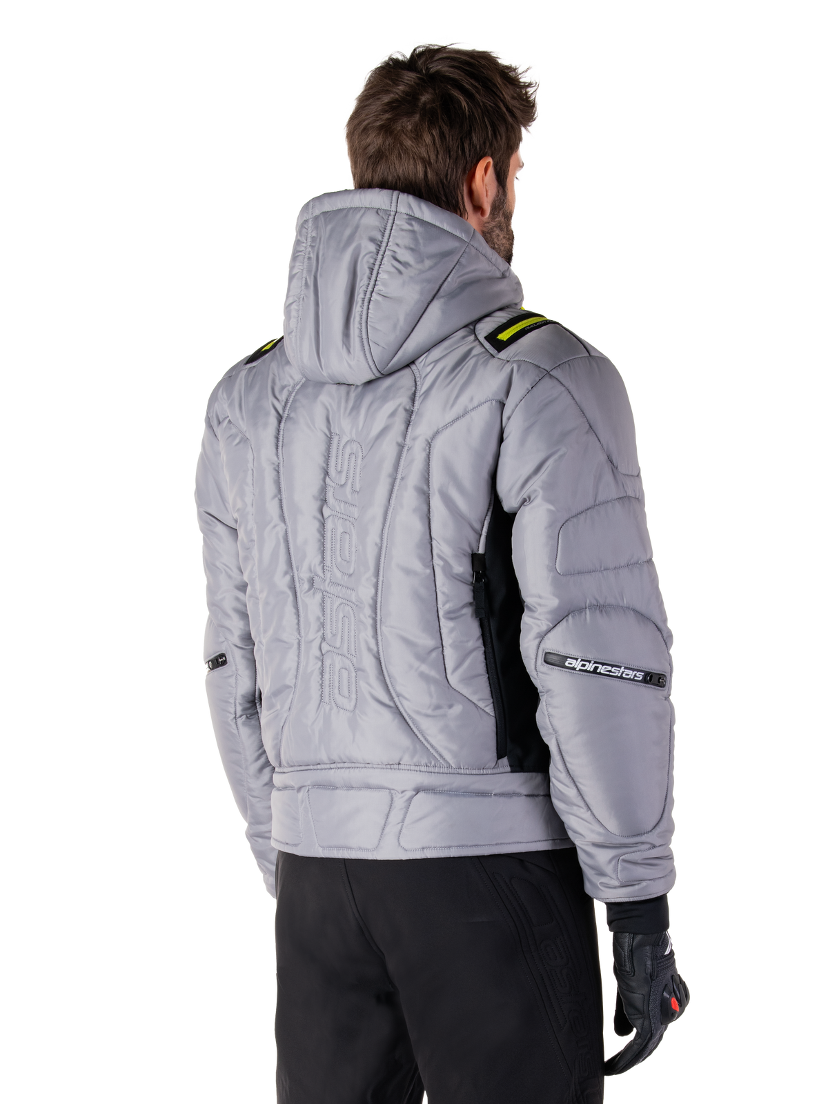 Alpinestars Mohobbs vandtæt jakke i Lunar Gray og Lime Punch, set bagfra på en model, quiltet polstret bomber-design med lodret præget astars-branding på ryggen, limegrønne detaljer på skuldrene, med hætte, båret med sorte motorcykelbukser og handsker