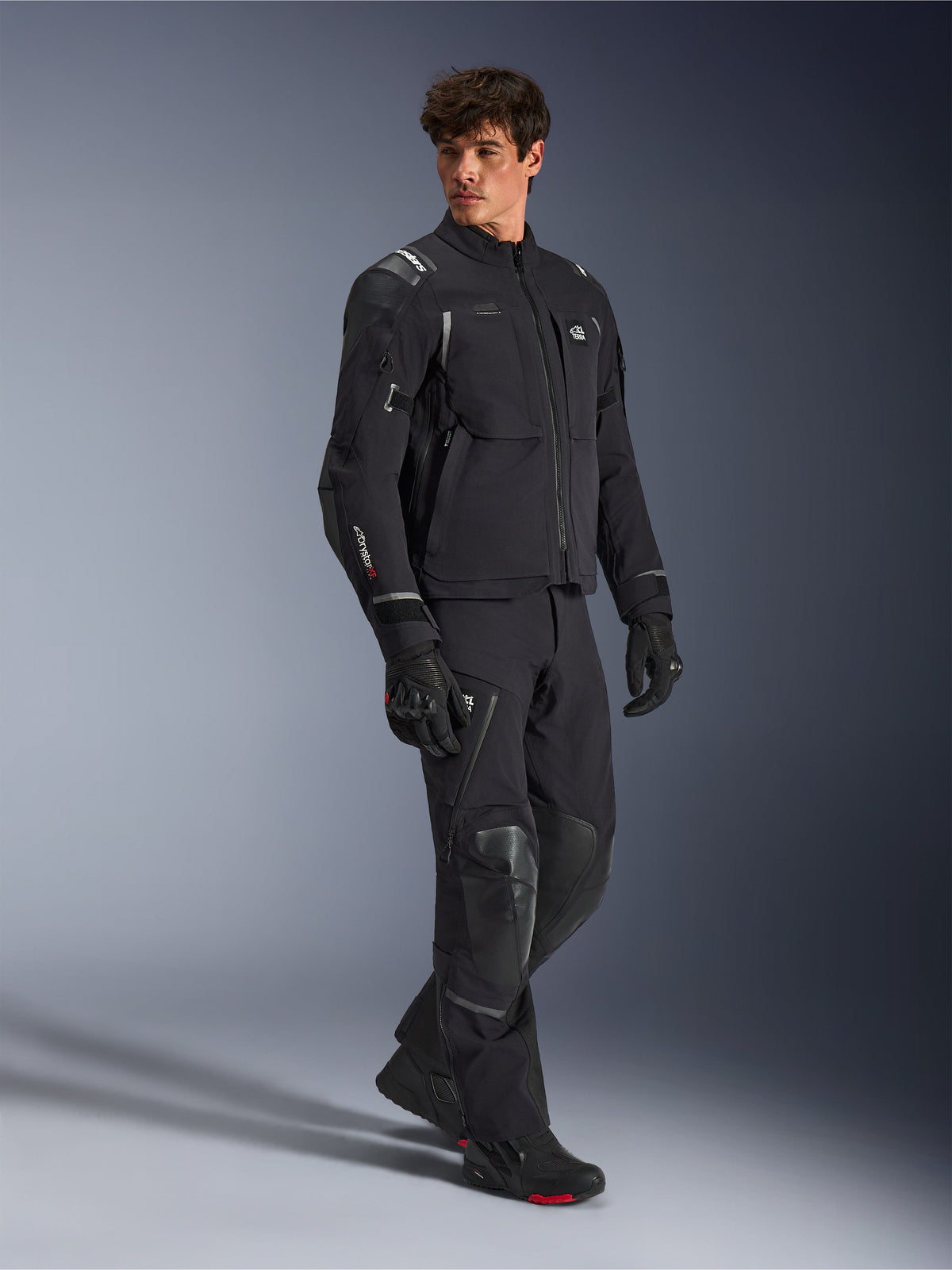 Alpinestars Andes Pro Drystar® XF Jacket, Black and Dark Gray motorcycle jacket, worn by male model with matching adventure pants, gloves, and boots, full-body studio shot, technical adventure touring gear with reflective details and branding