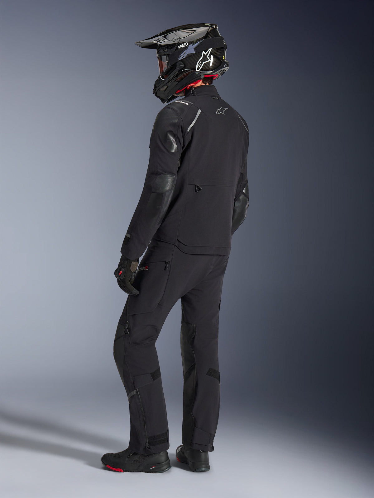 Motorcyclist wearing the Alpinestars Andes Pro Drystar® XF Jacket and matching pants in Black and Dark Gray, back view profile, featuring a black carbon-fiber adventure helmet, black gloves, and adventure boots, high-performance coordinated gear for adventure touring.