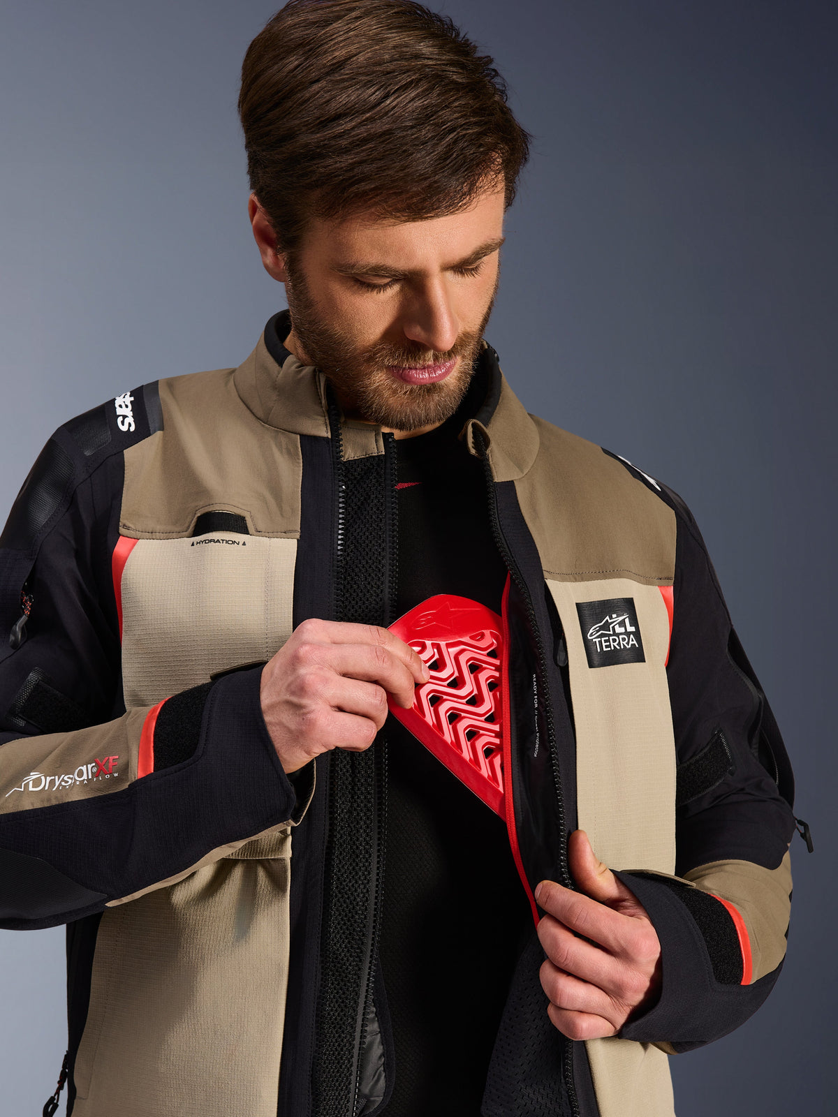 Alpinestars Andes Pro Drysta r® XF-jakke i Walnu t Aluminu m, model demonstrere r den røde Nucleo n-brystbe skytter-i ndsats i den indve ndige lo mme, adve nture mo torcykelj akke med ALL TERR A-brandin g og Drys tar XF-lo goer.