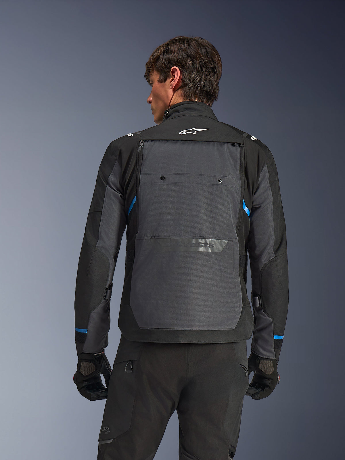 Alpinestars Cusco Drystar®-jakke, motorcykeljakke, sort og mørkegrå, set bagfra på en model, viser stort gråt rygpanel, hvidt Alpinestars-logo og blå detaljer på ærmerne