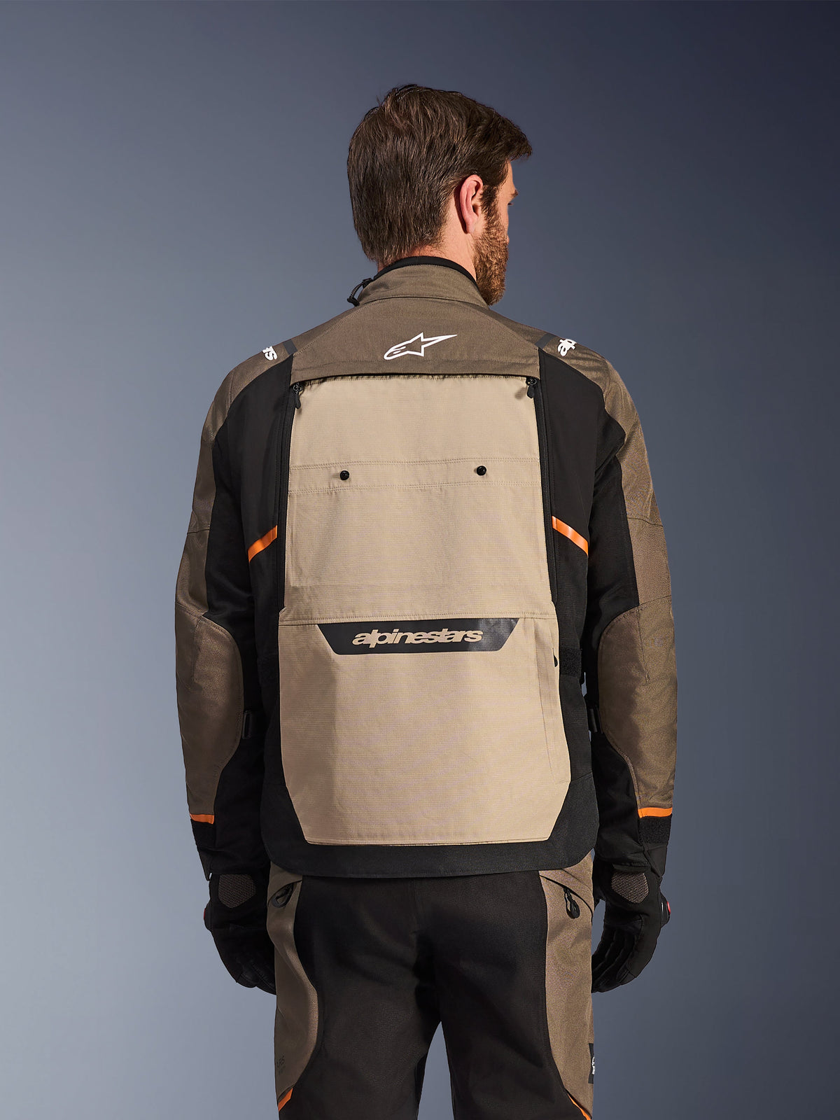Alpinestars Cusco Drystar® jakke, Walnut Aluminum Black, set bagfra, med et stort sandfarvet rygpanel og sort logo, orange detaljer, bæres med matchende bukser og handsker, designet til adventure touring