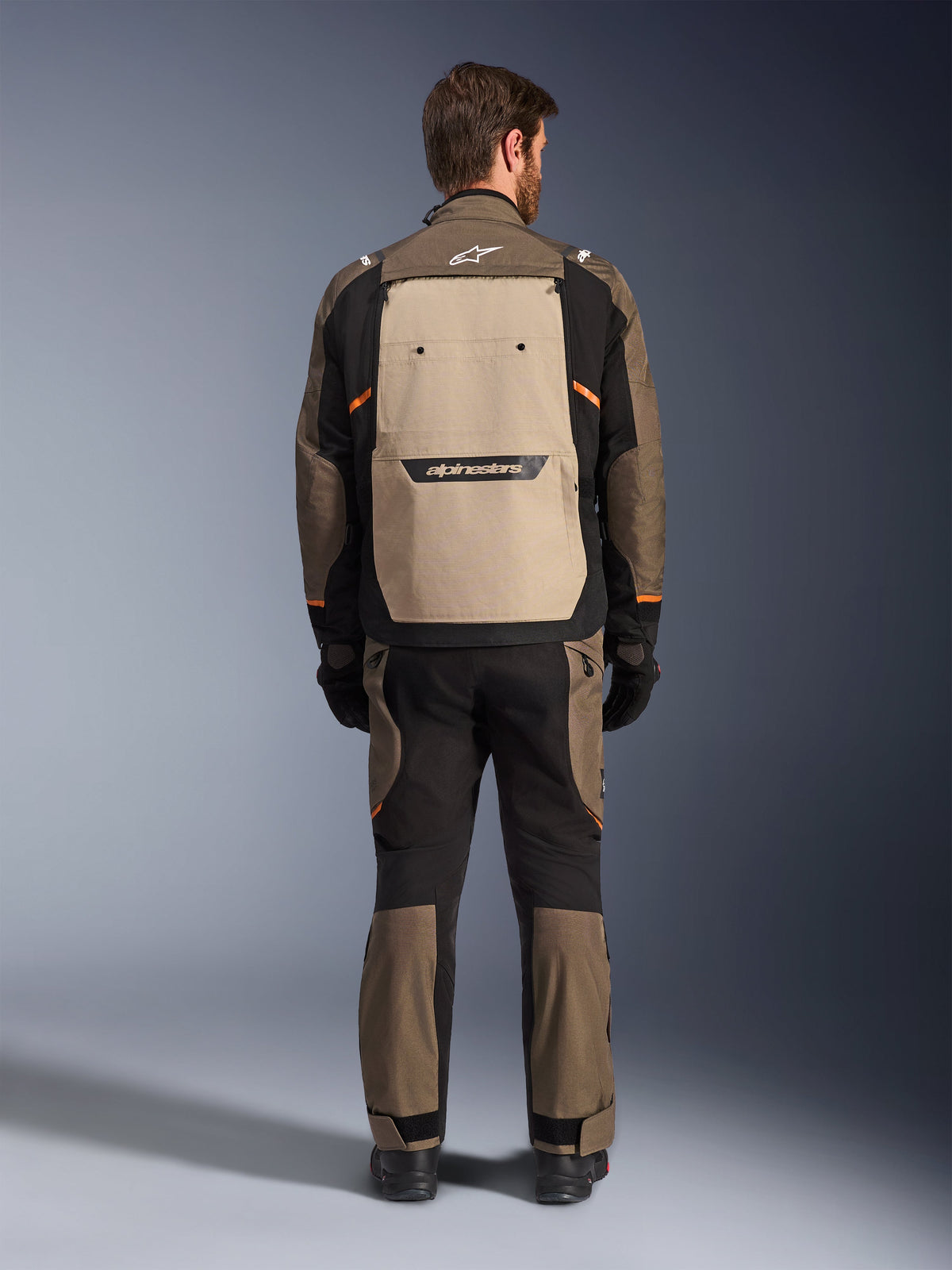 Alpinestars Cusco Drystar® jakke, set bagfra, Walnut Aluminum Black, tekstil adventure touring-udstyr, stort sandfarvet ventilationspanel på ryggen med sort branding, orange detaljer, båret med matchende bukser og handsker