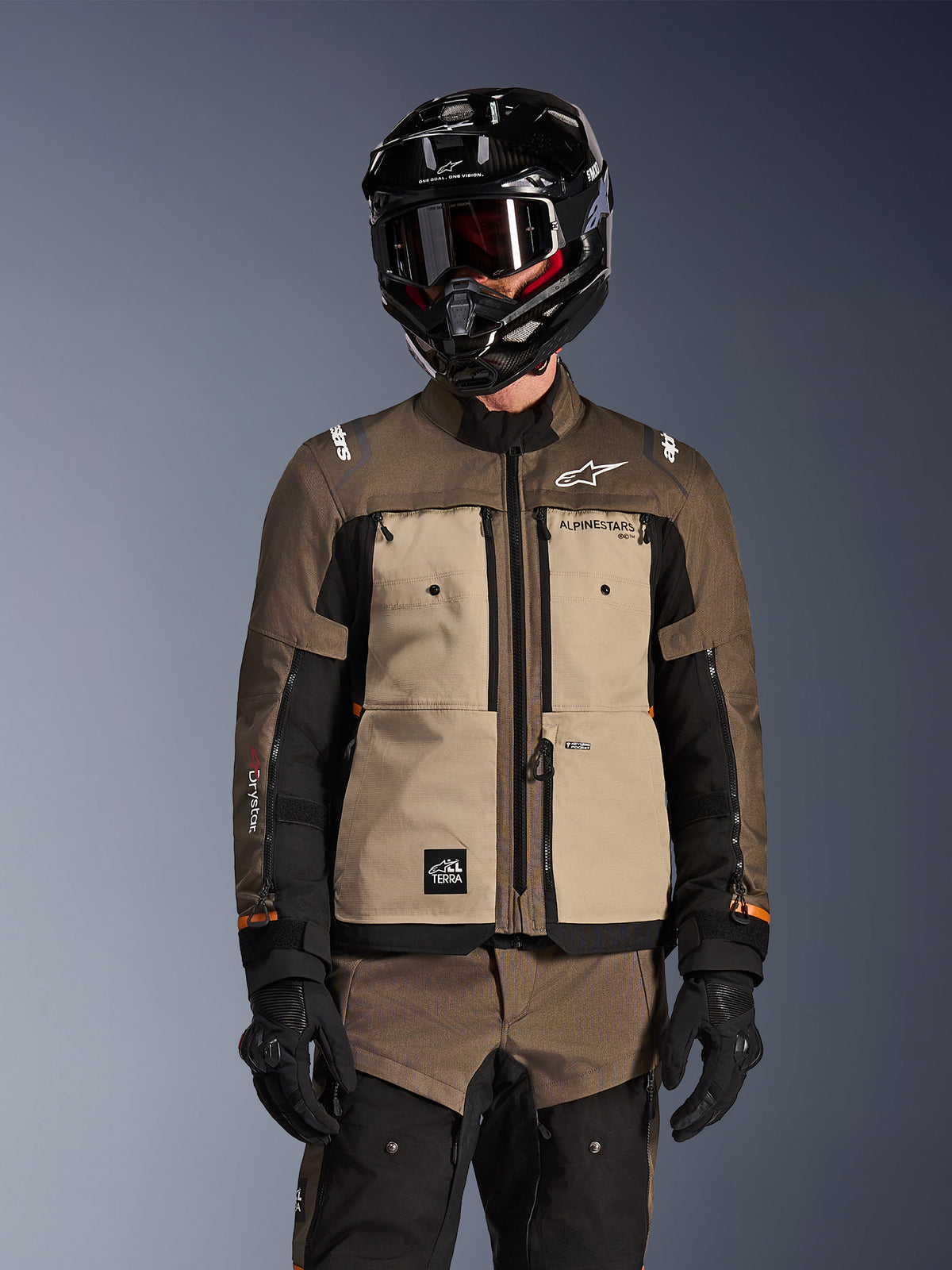 Motorcykelkører iført Alpinestars Cusco Drystar Jakke i Walnut Aluminum Black, adventure touring motorcykelsæt med sort hjelm med goggles og sorte handsker, frontvisning der viser den tekniske tekstilkonstruktion, lommer og branding.
