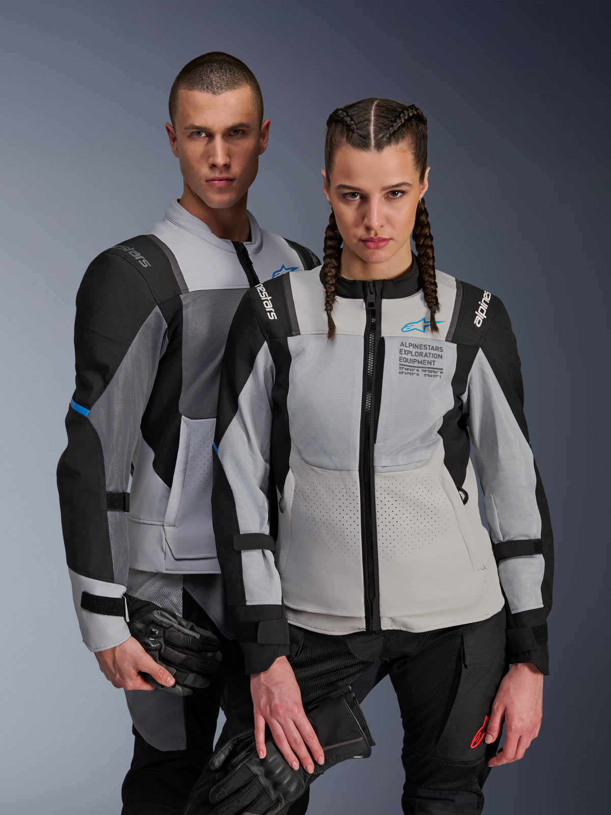 Alpinestars ST-2 Air jakker, tekstil motorcykeljakker, isgrå, mørkegrå og sort, par iført matchende adventure touring-udstyr med mesh-ventilationspaneler og Alpinestars Exploration Equipment-branding, holder motorcykelhandsker