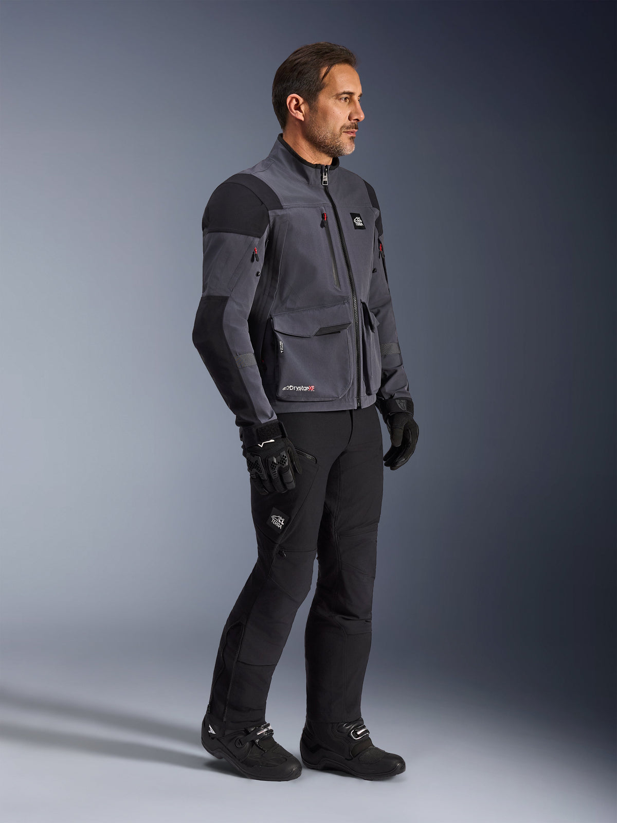 Alpinestars Maxdura Drystar®XF Laminated Armored Shell, mørkegrå og sort motorcykeljakke, teknisk dual-sport skal båret med matchende sorte bukser og støvler, med cargolommer og forstærkede skulderpaneler, studiebillede af komplet adventure-køreudstyr
