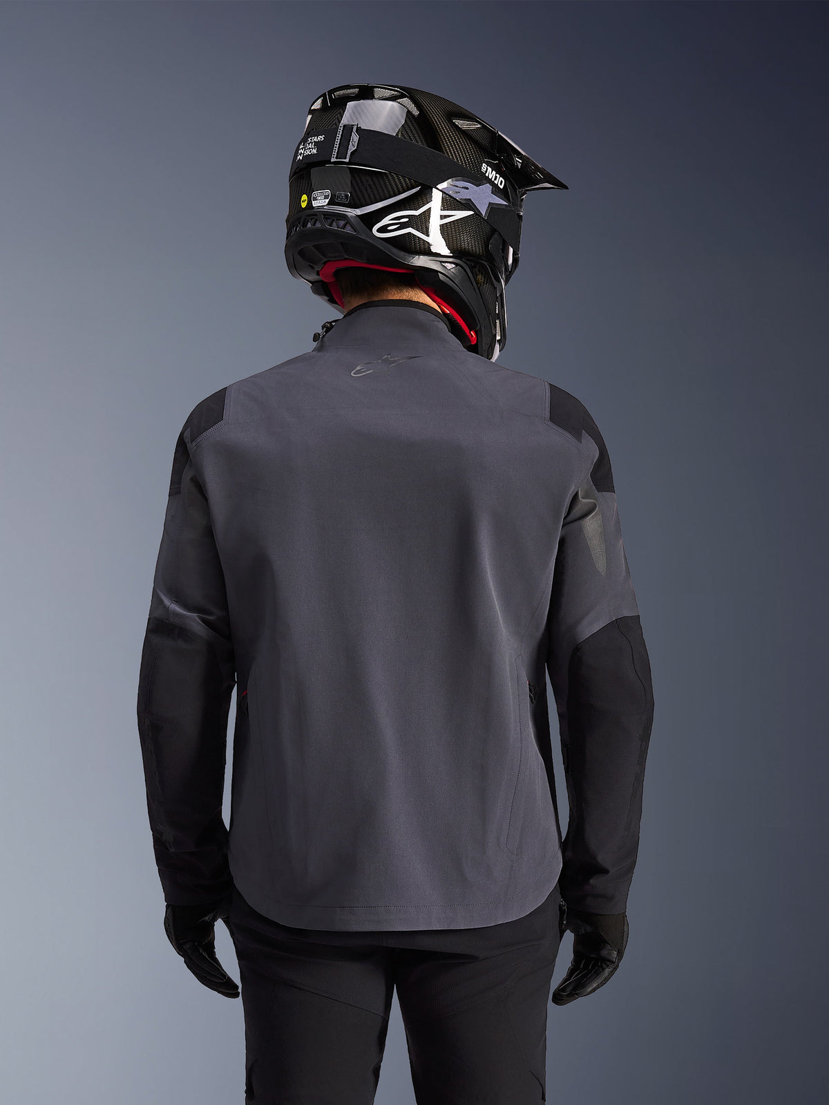 Alpinestars Maxdura Drystar®XF Laminated Armored Shell, adventure motorcykeljakke, Deep Gray Black, set bagfra med fokus på den tekniske tekstilkonstruktion og forstærkede paneler, båret med sort kulfiberhjelm, sorte kørebukser og handsker
