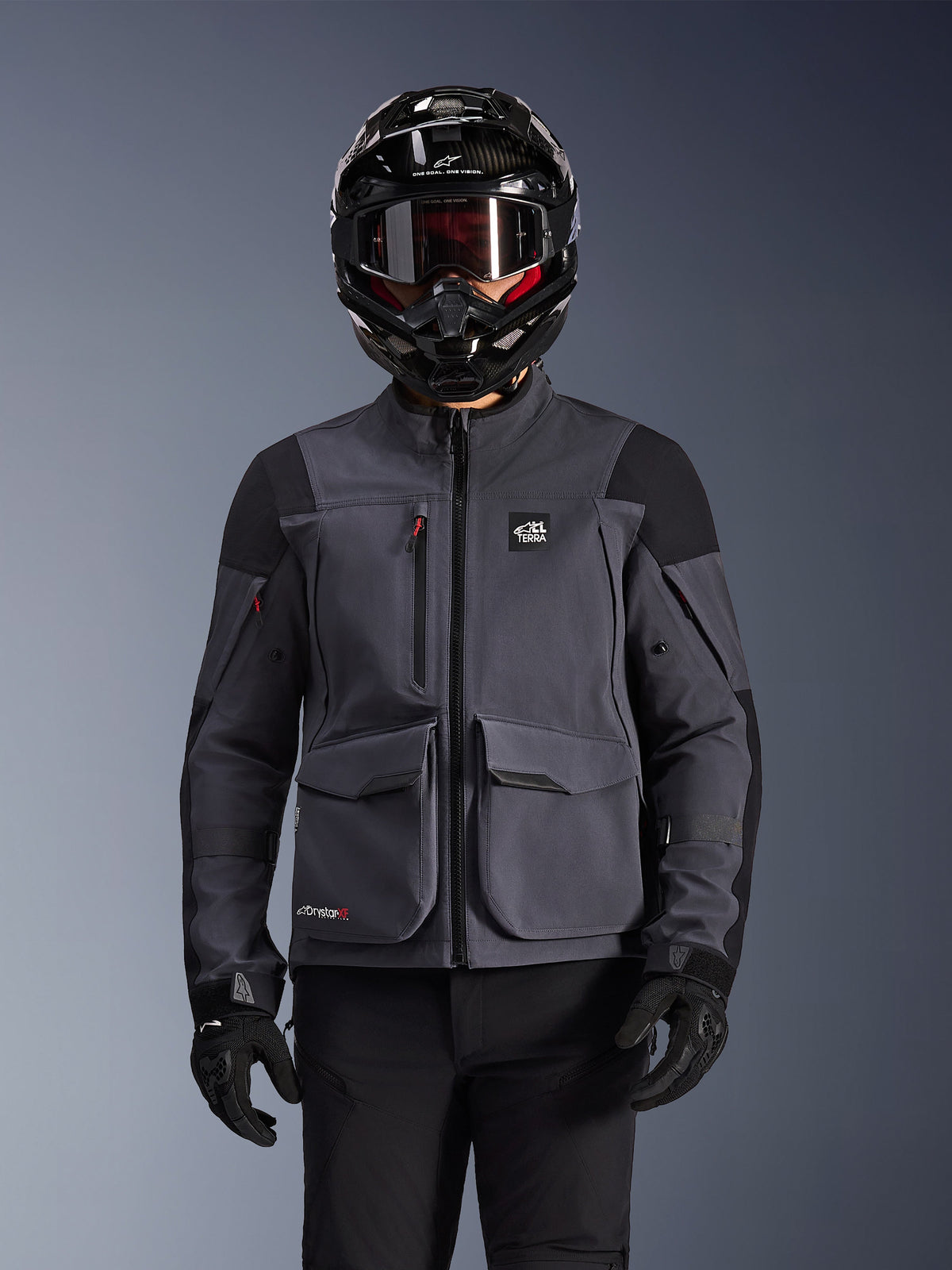 Alpinestars Maxdura Drystar®XF Laminated Armored Shell, motorcykeljakke, mørkegrå og sort, bæres af en kører med sort hjelm, briller og handsker, med store tekniske cargo-lommer og ALL TERRA-branding, adventure touring-udstyr