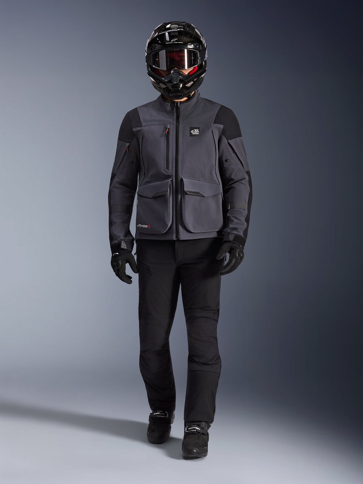 Alpinestars Maxdura Drystar®XF Laminated Armored Shell, adventure-motorcykeljakke i Deep Gray og sort, båret med matchende sorte kørebukser, en sort full-face hjelm, handsker og støvler, med fremtrædende cargo-lommer og ALL TERRA-branding for et teknisk off-road touring-look
