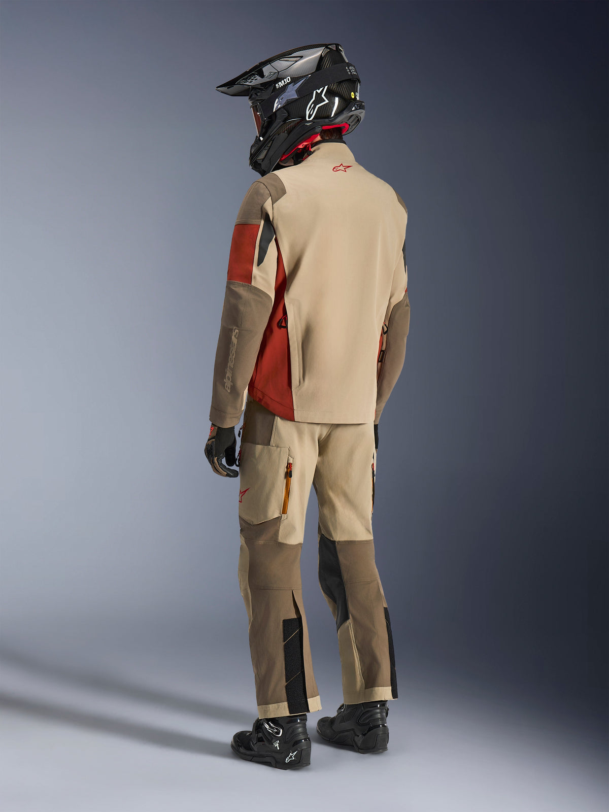 Adventure rider from the back wearing the Alpinestars Maxdura Drystar®XF Laminated Armored Shell in Aluminum Walnut Rust Brown, paired with matching riding pants, black off-road helmet, and black boots, complete technical touring outfit.