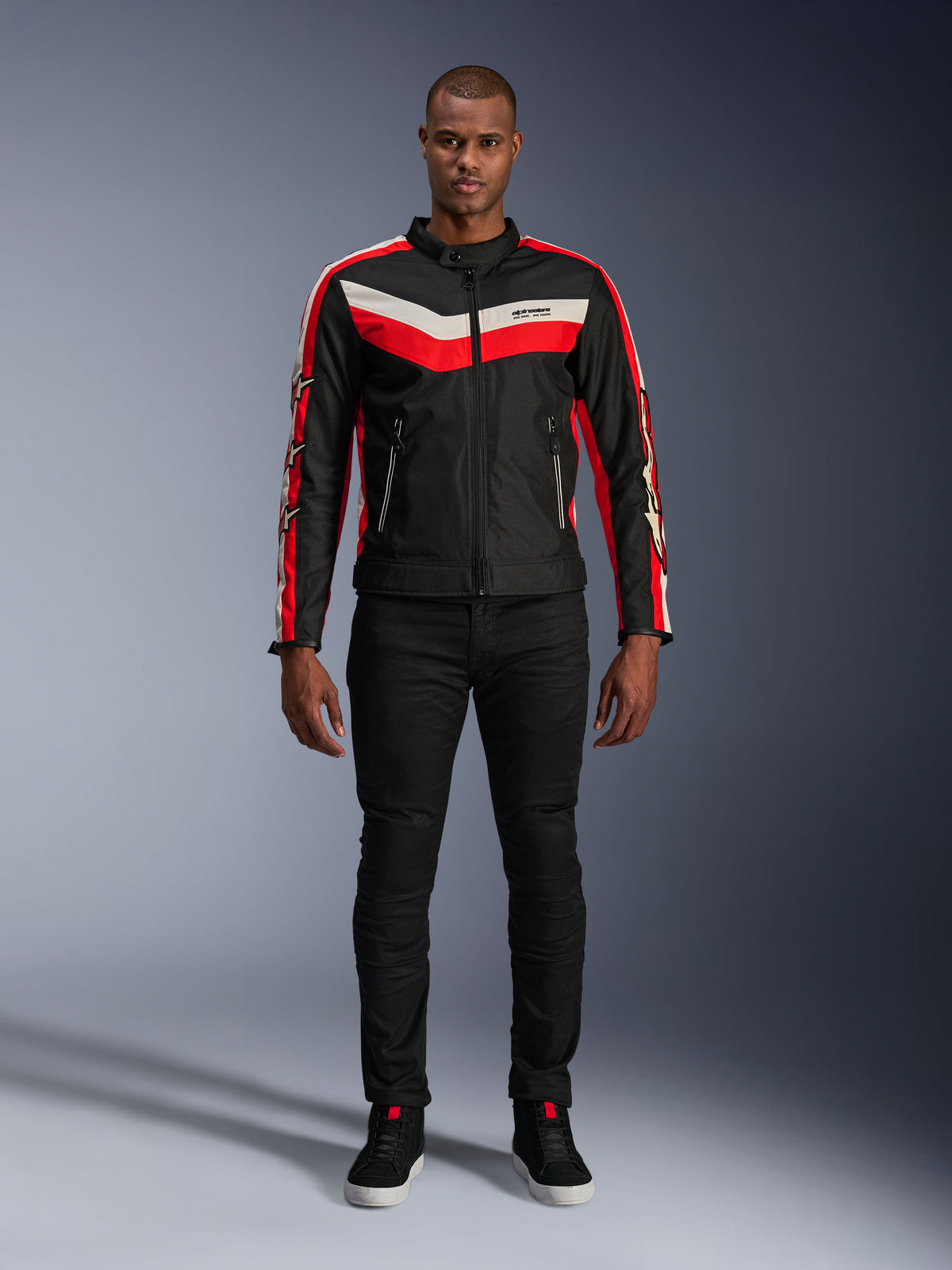 Alpinestars T-Dyno WR-jakke, tekstilmotorcykeljakke i sort, klar rød og ecru, med V-formede bryststriber og stjerne-branding på ærmerne, båret med sorte bukser og sorte køresko, heritage-inspireret urbant udstyr