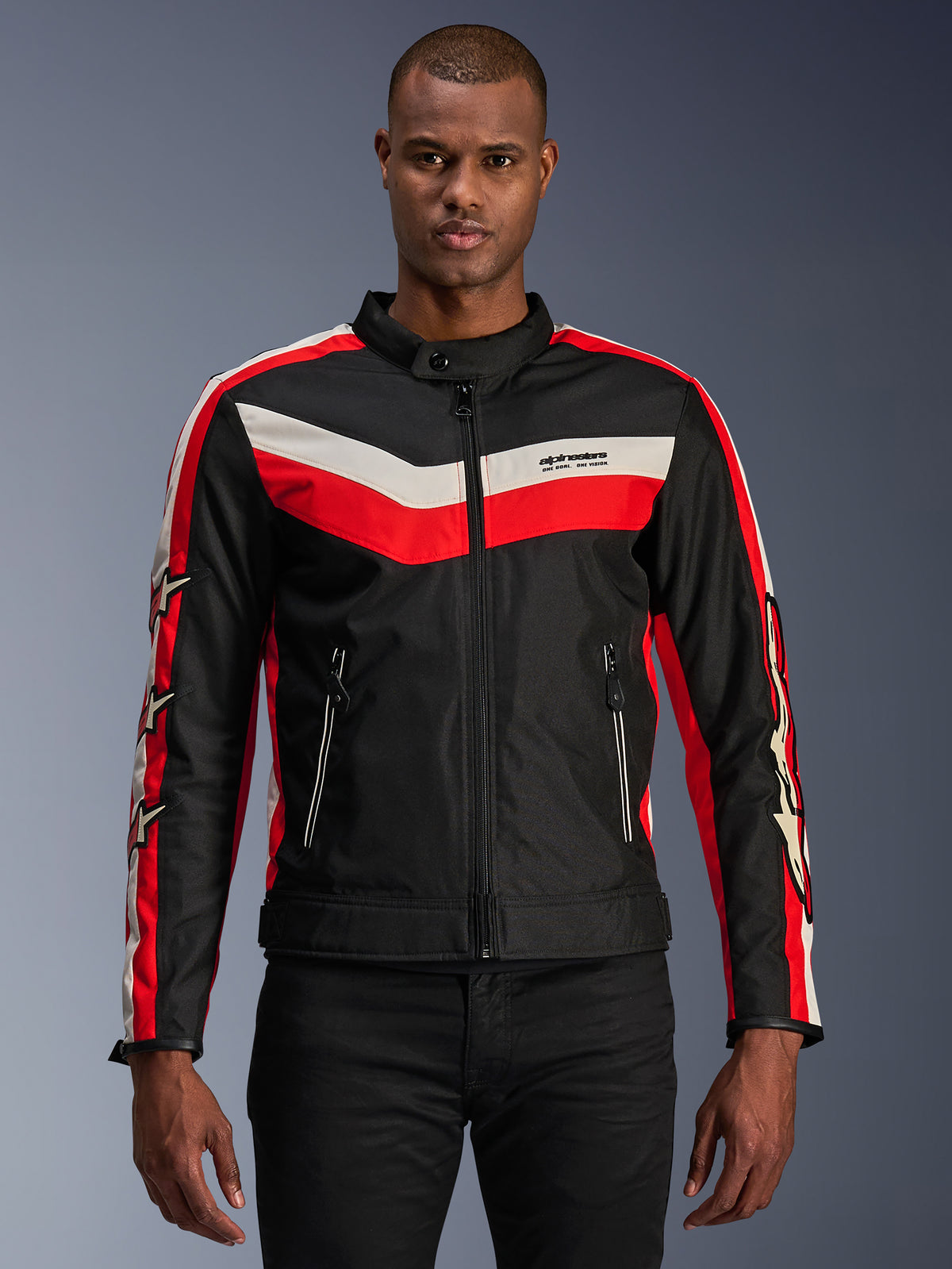 Alpinestars T-Dyno WR-jakke, tekstil motorcykeljakke, sort med klare røde og ecru chevron-striber, vintage-inspireret biker-pasform, høj krave med knaplukning, lynlåslommer foran, stjernelogoer på ærmerne, båret af model