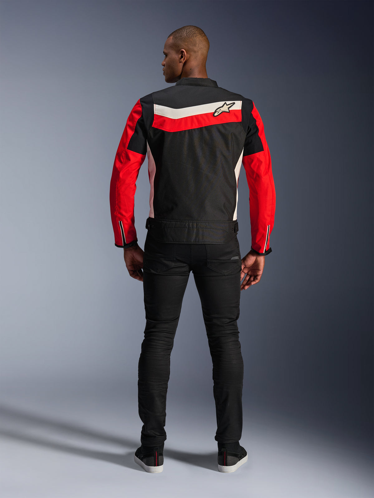 Alpinestars T-Dyno WR Jakke, tekstilmotorcykeljakke, sort, klar rød og ecru, set bagfra med horisontale rygstriber og røde ærmer, vintage-inspireret bikerpasform, båret med sorte bukser, urbant vej-køreudstyr