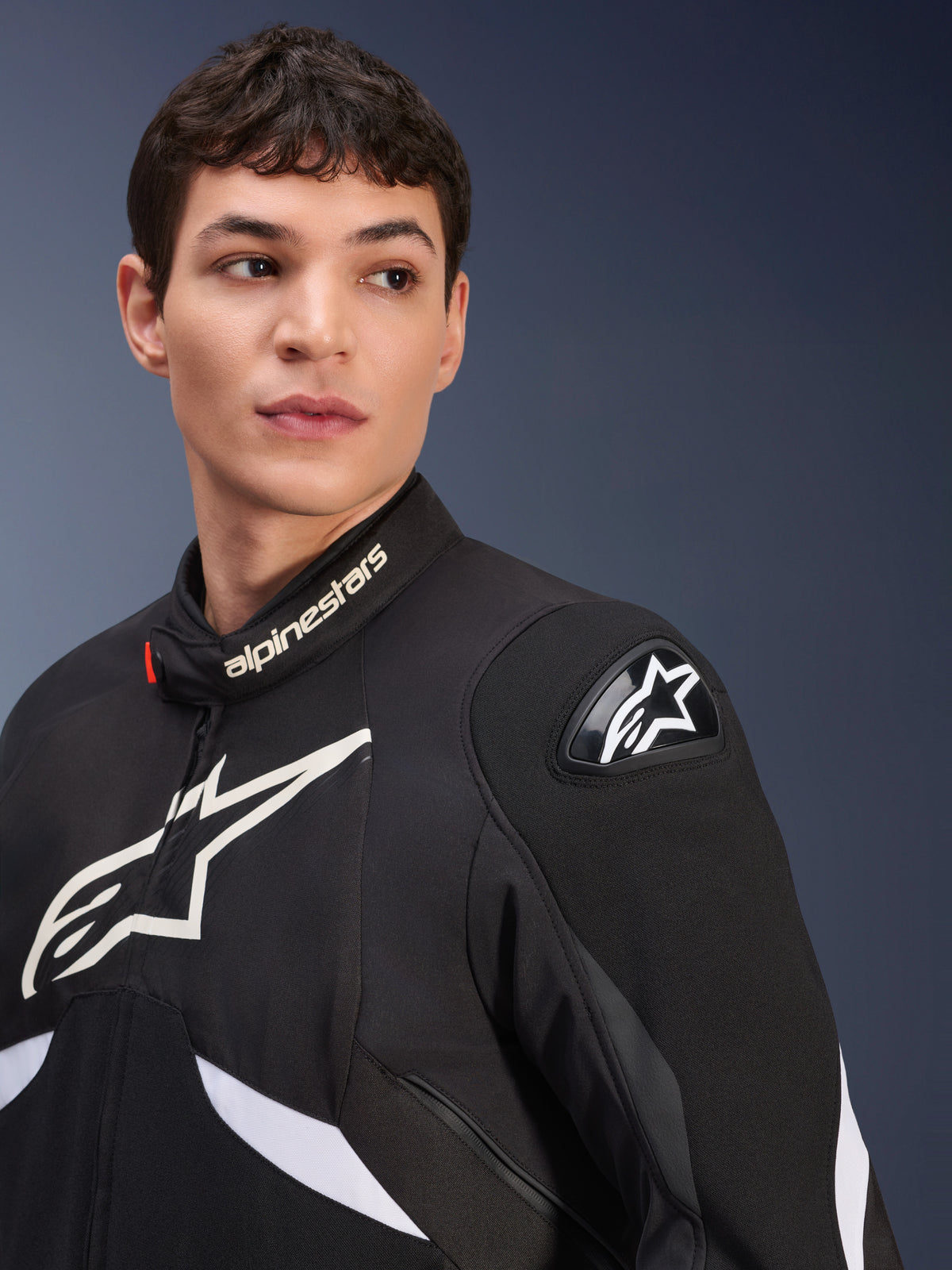 Alpinestars T-GP R V3 Drystar® jakke, sort og hvid, vist på en mandlig model, hvide Alpinestars-logoer på krave og bryst, sort DFS-skulder-slider med en hvid stjerne, detaljeret lifestyle-billede af en vandtæt sportstekstiljakke
