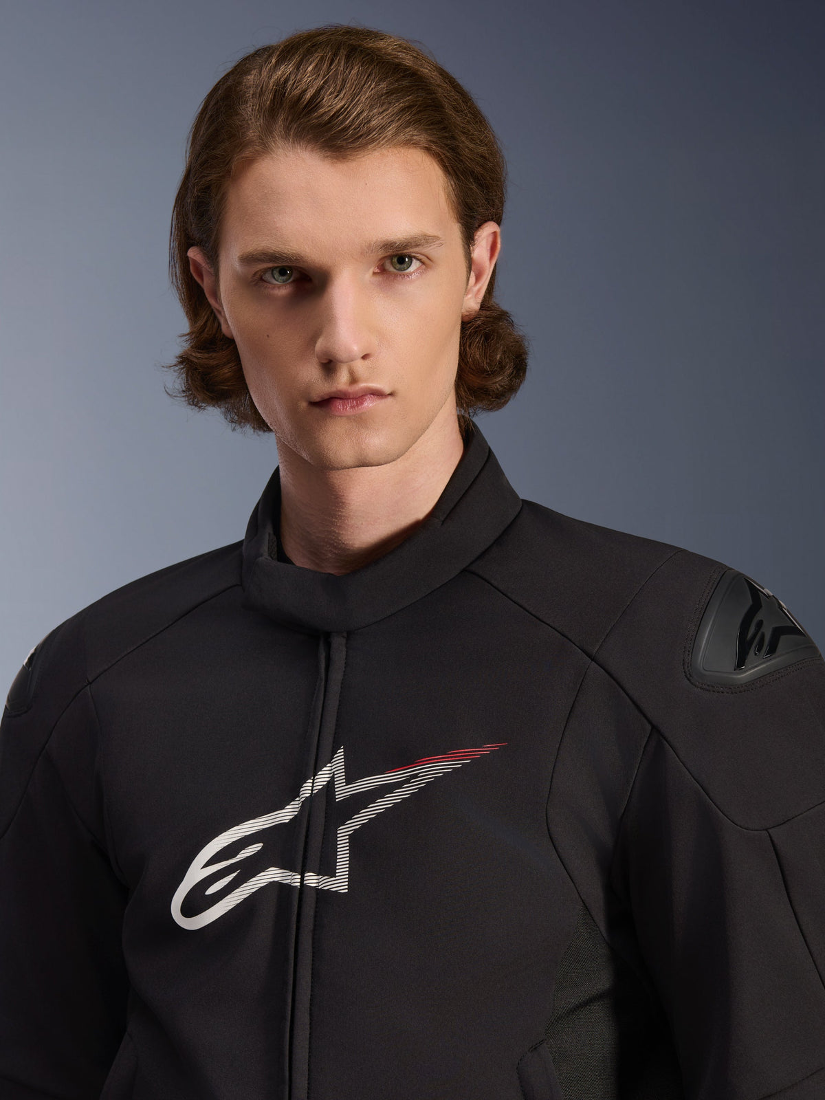 Model iført Alpinestars SMX Waterproof Jacket, sort med hvide og Bright Red detaljer, med et stort hvidt stjernelogo med en rød stribe på brystet, DFS Lite skulderbeskyttere og en strømlinet tekstilkonstruktion til motorcykelkørsel på vej.